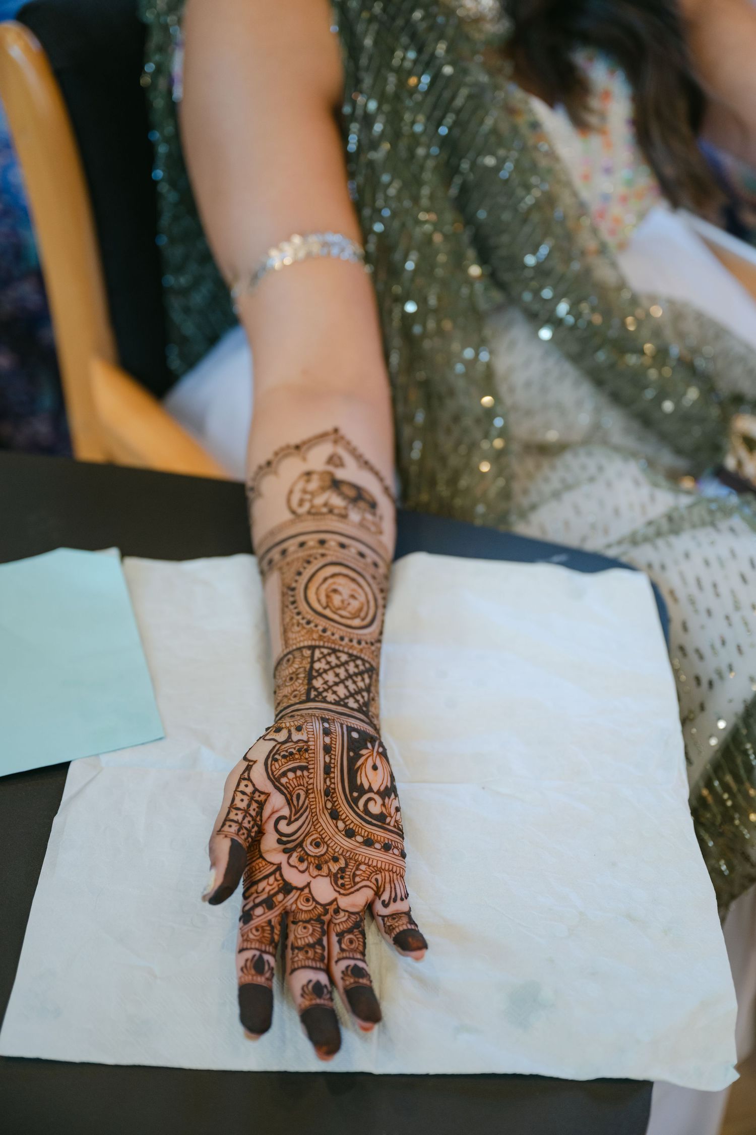 The Brix on the Fox Wedding - Intricate henna design decorates an arm resting on white paper with sparkly fabric visible in the background.
