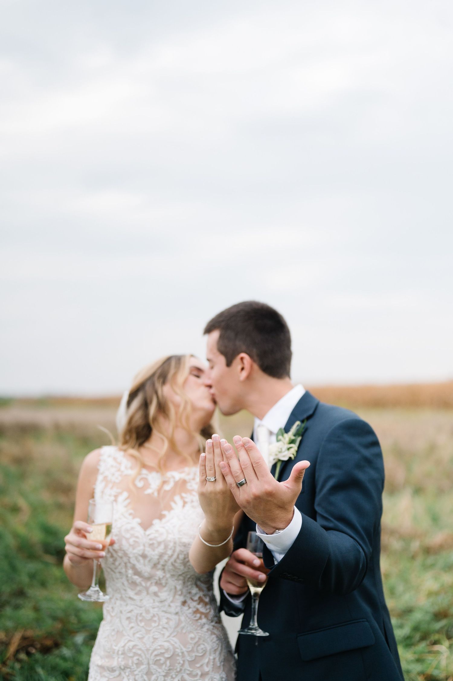 A bride and groom share a romantic toast with champagne glasses in an outdoor field setting. - Ashley Farm in Yorkville