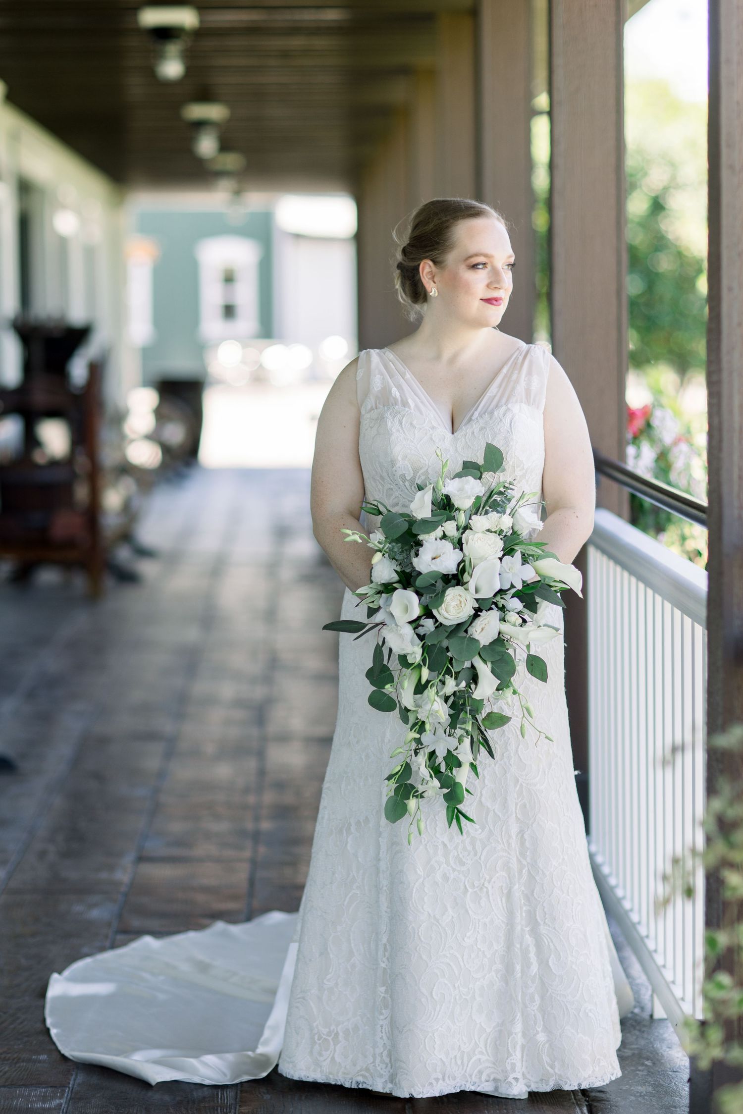 Beautiful bridal portrait on a covered porch featuring a classic white lace gown and cascading white bouquet. - Kuiper's Family Farm Wedding