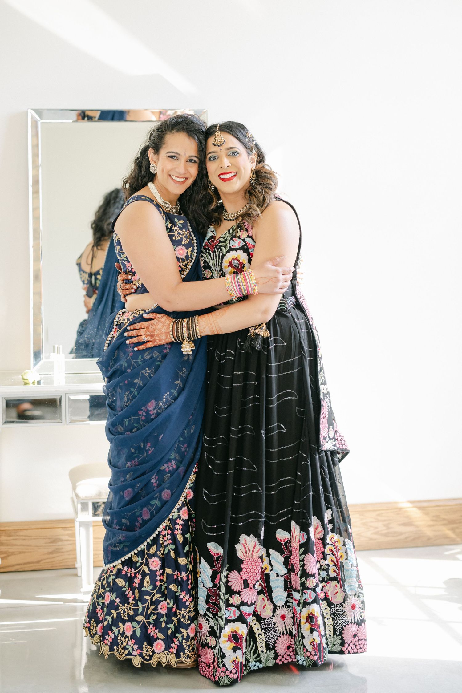 Two friends in floral dresses share a joyful embrace while posing together in a bright indoor setting. - The Brix on the Fox