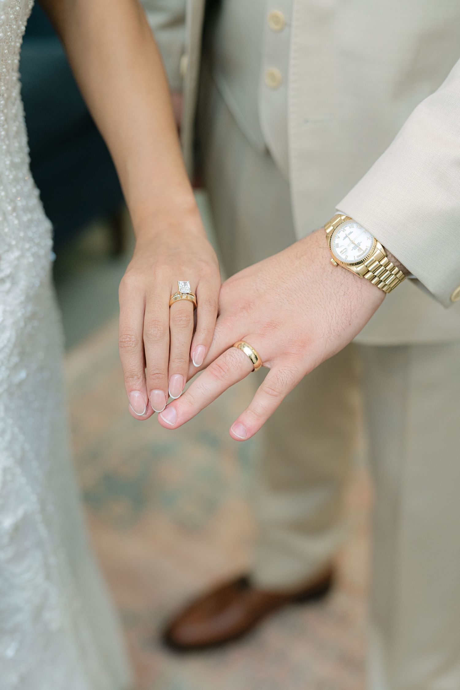 The BRIX on the Fox Wedding - Close-up view of hands wearing gold wedding rings and watches against a light background.