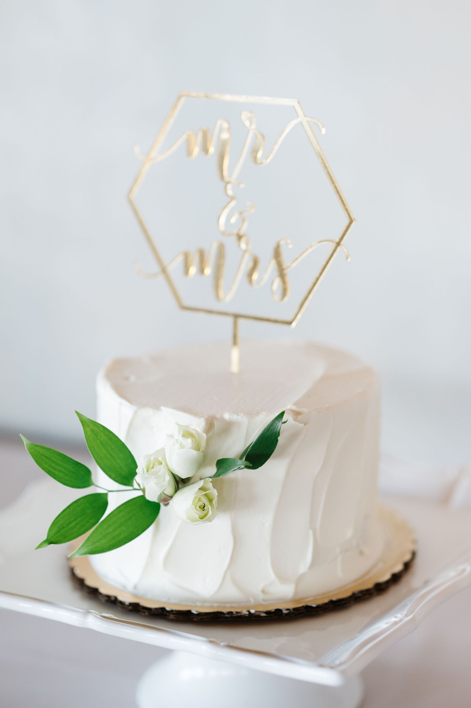 White wedding cake with gold 'Mr & Mrs' topper and white rose decoration.