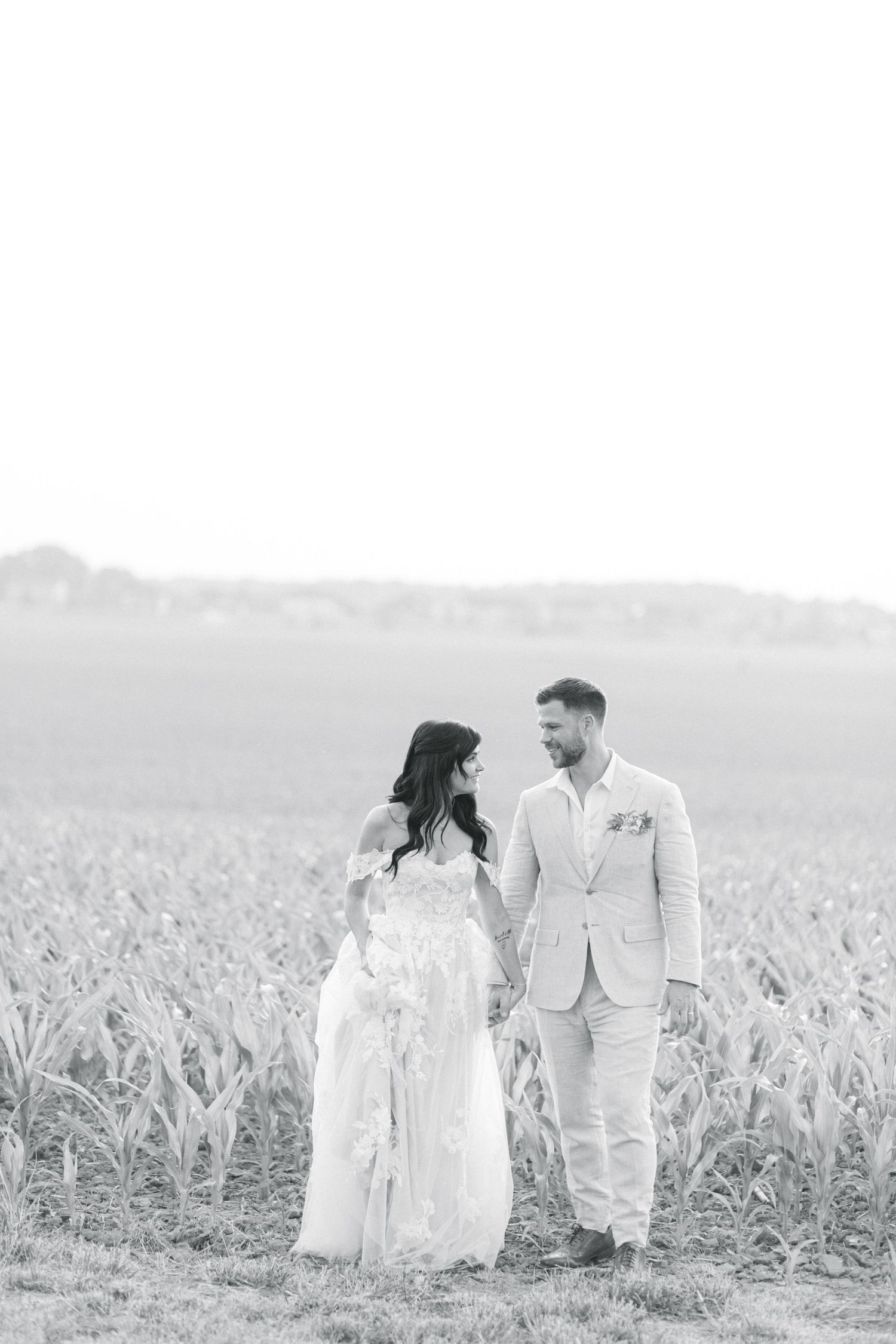 Black and white photo of a couple standing in a cornfield wearing elegant wedding attire. - Venue 5126