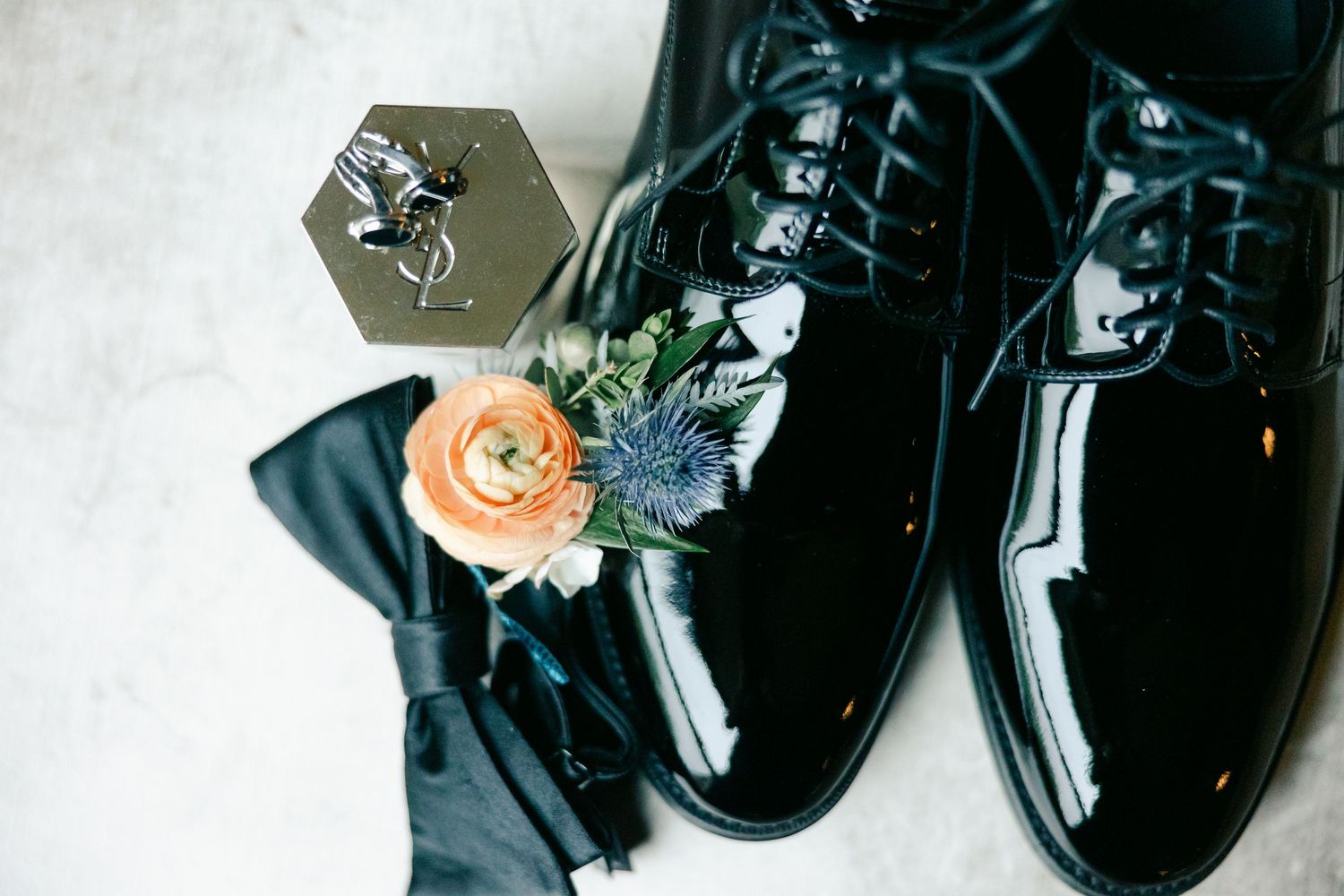 A pair of shiny black patent leather dress shoes with peach colored roses and greenery arranged on top. - Hyatt Lodge Oak Brook