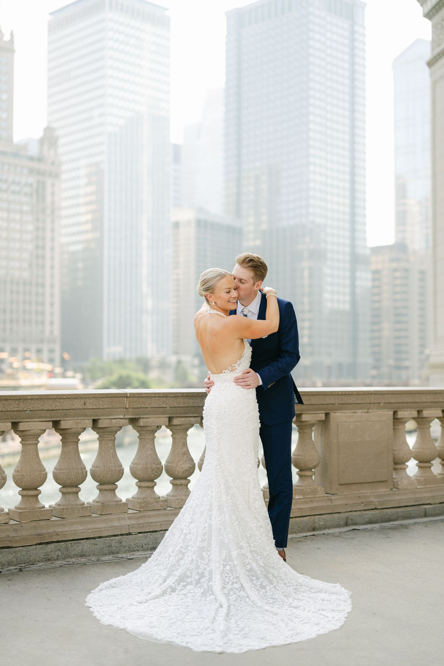 Newlyweds embrace on city balcony with stunning architectural backdrop.