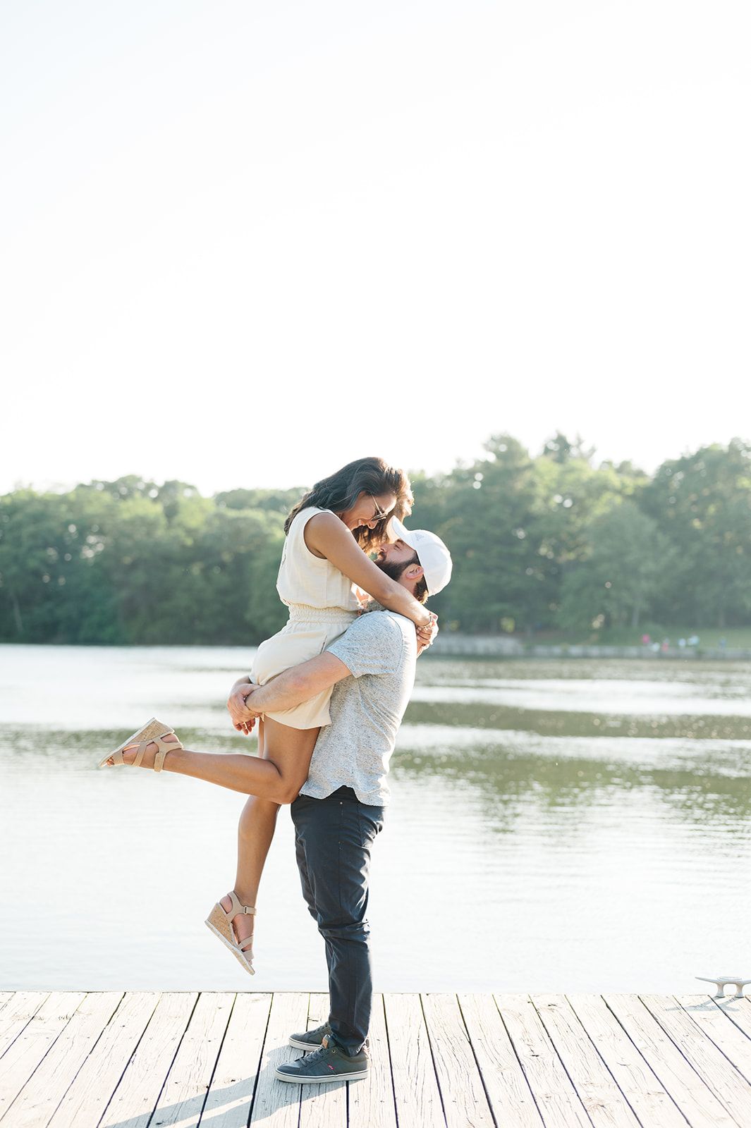 Couple sharing a romantic embrace on a wooden dock by a lake, man lifting woman in a joyful hug outdoors. - Wheaton Engagement Session