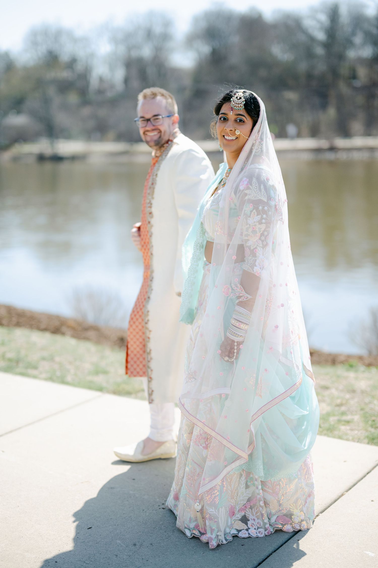 A couple in elegant wedding attire sits by a serene lake, with the bride wearing a flowing white and mint green dress. - The Brix on the Fox