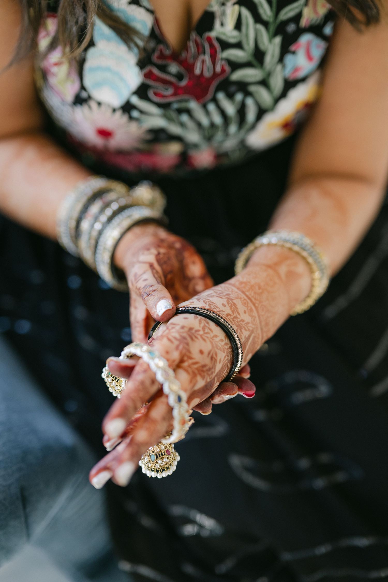 Hands adorned with intricate henna designs and bangles hold a decorative ring during a traditional wedding ceremony. - The Brix on the Fox