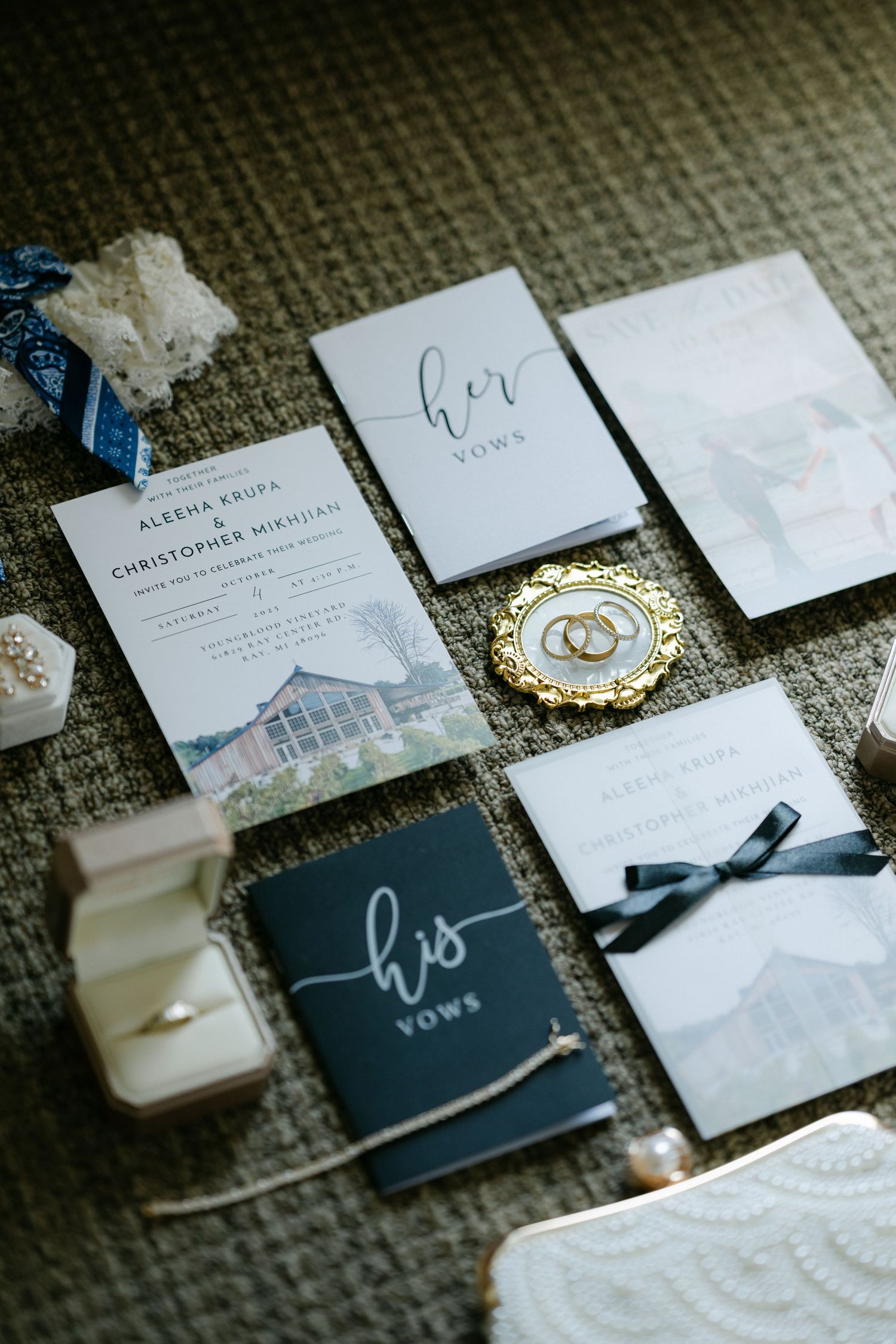 Elegant wedding flat lay featuring vow books, invitation suite, gold rings, and bridal accessories on neutral background.