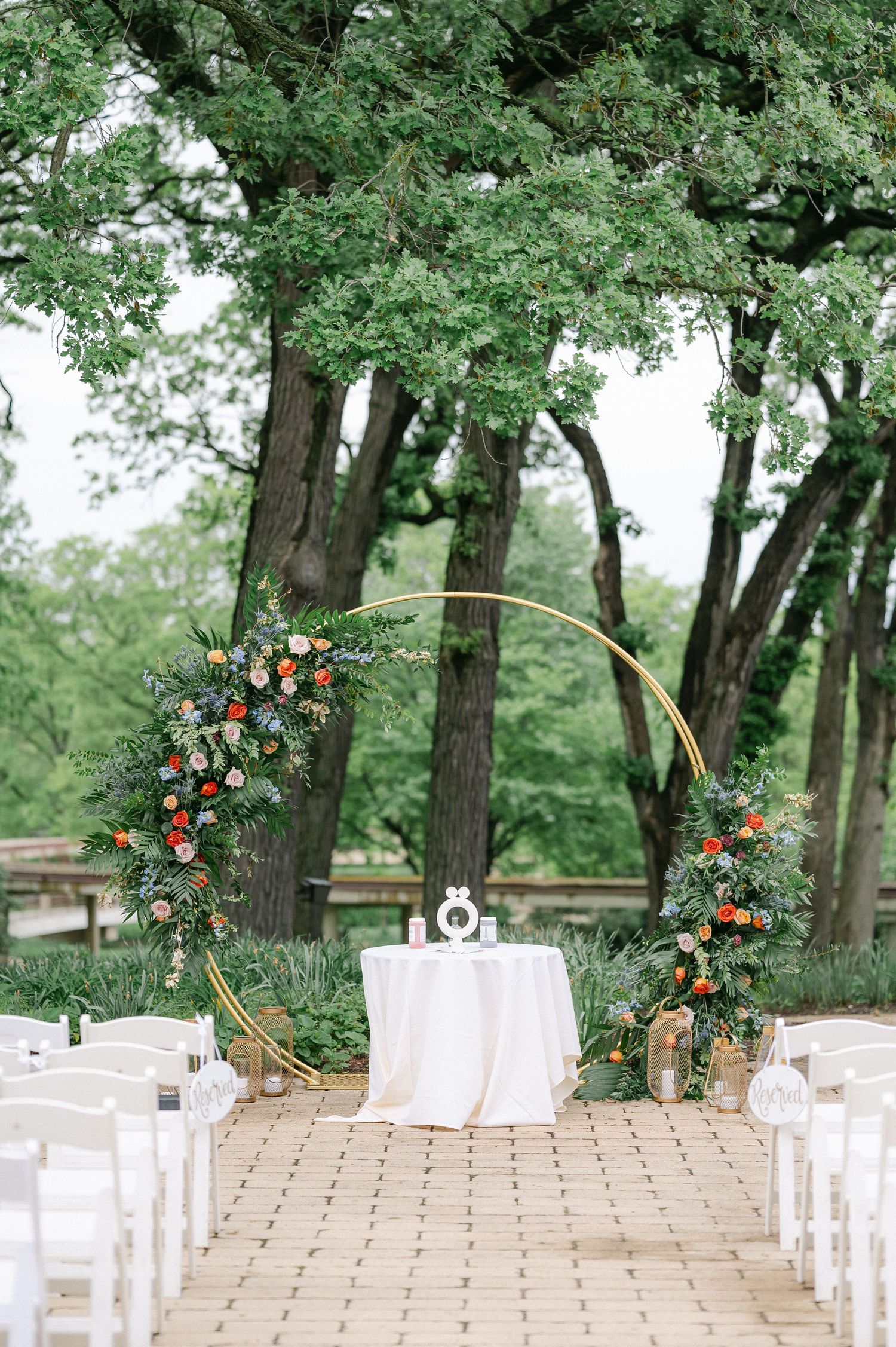 Outdoor wedding ceremony setup with gold arch decorated with orange and green florals on stone path. - Hyatt Lodge Oak Brook Wedding