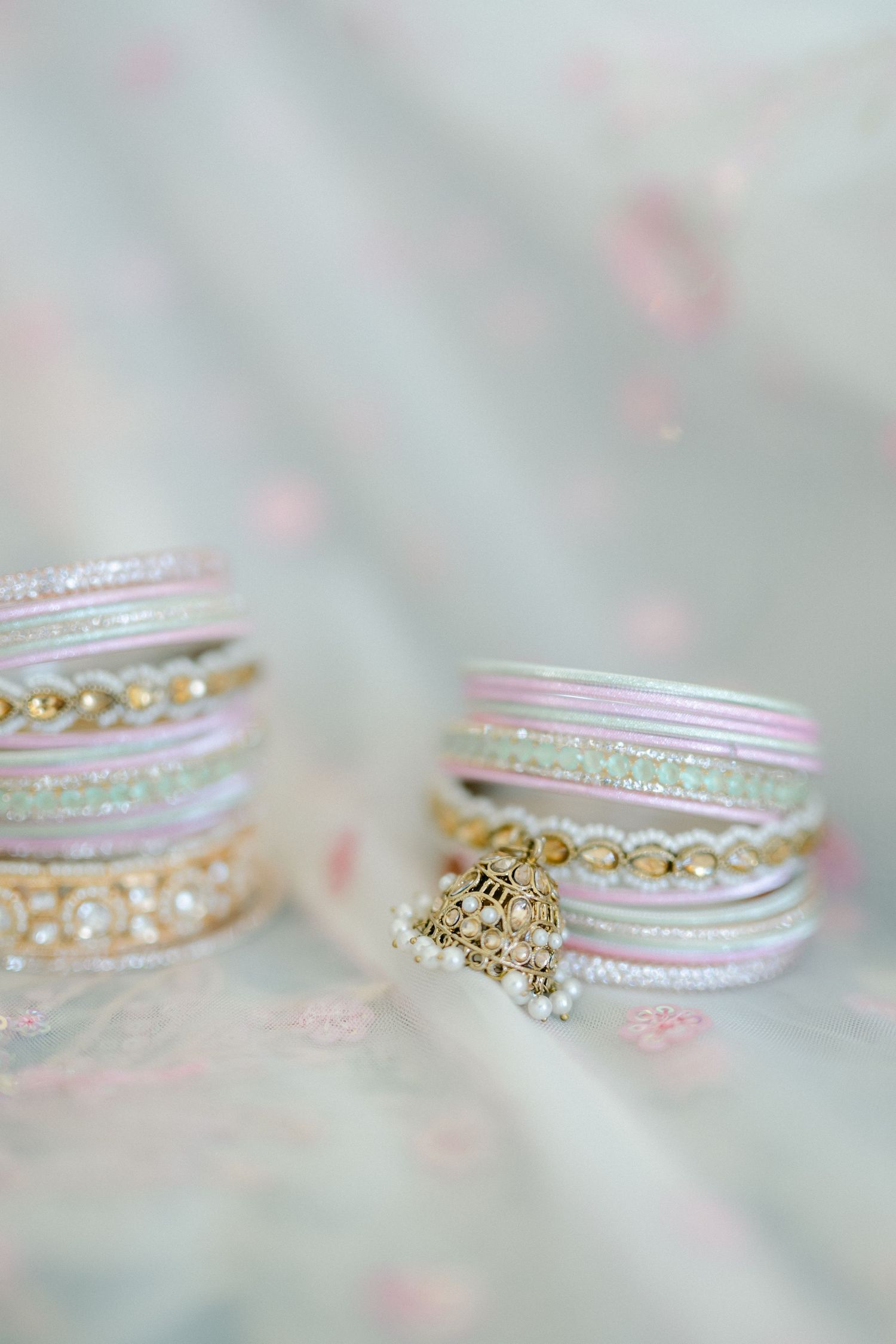 Delicate pink and gold bangles with pearl details arranged on soft floral fabric in pastel tones. - The Brix on the Fox