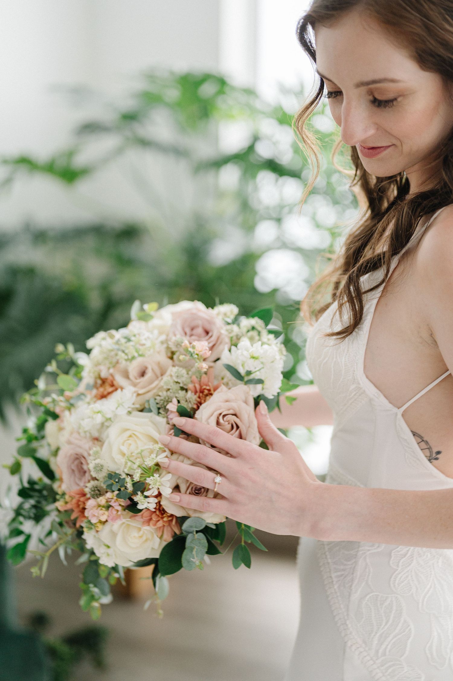 Close-up of bride holding soft pink and white floral bouquet with greenery accents.