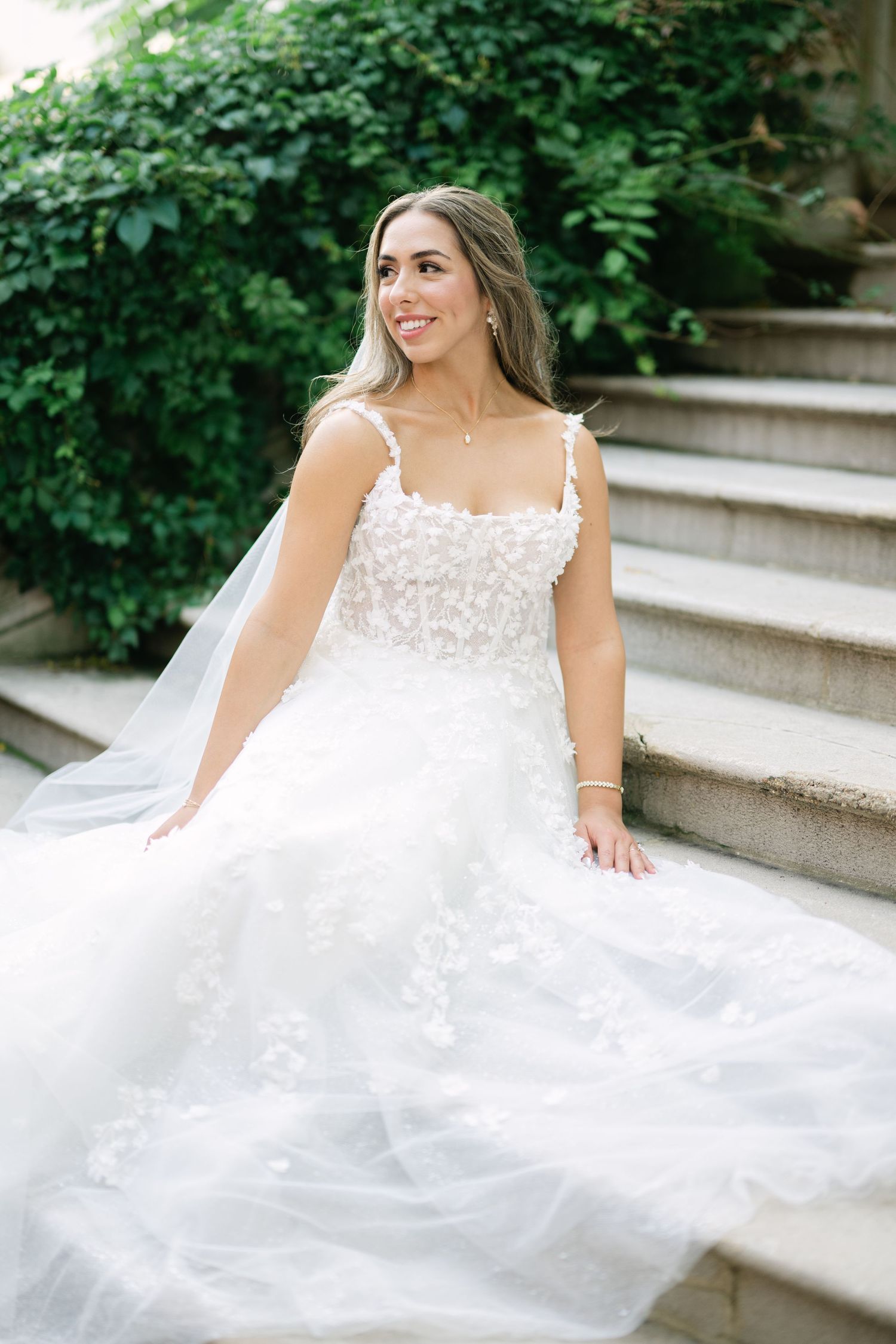 Beautiful wedding dress with lace bodice and flowing tulle skirt photographed on outdoor stone steps with greenery. - Meyer's Castle Events
