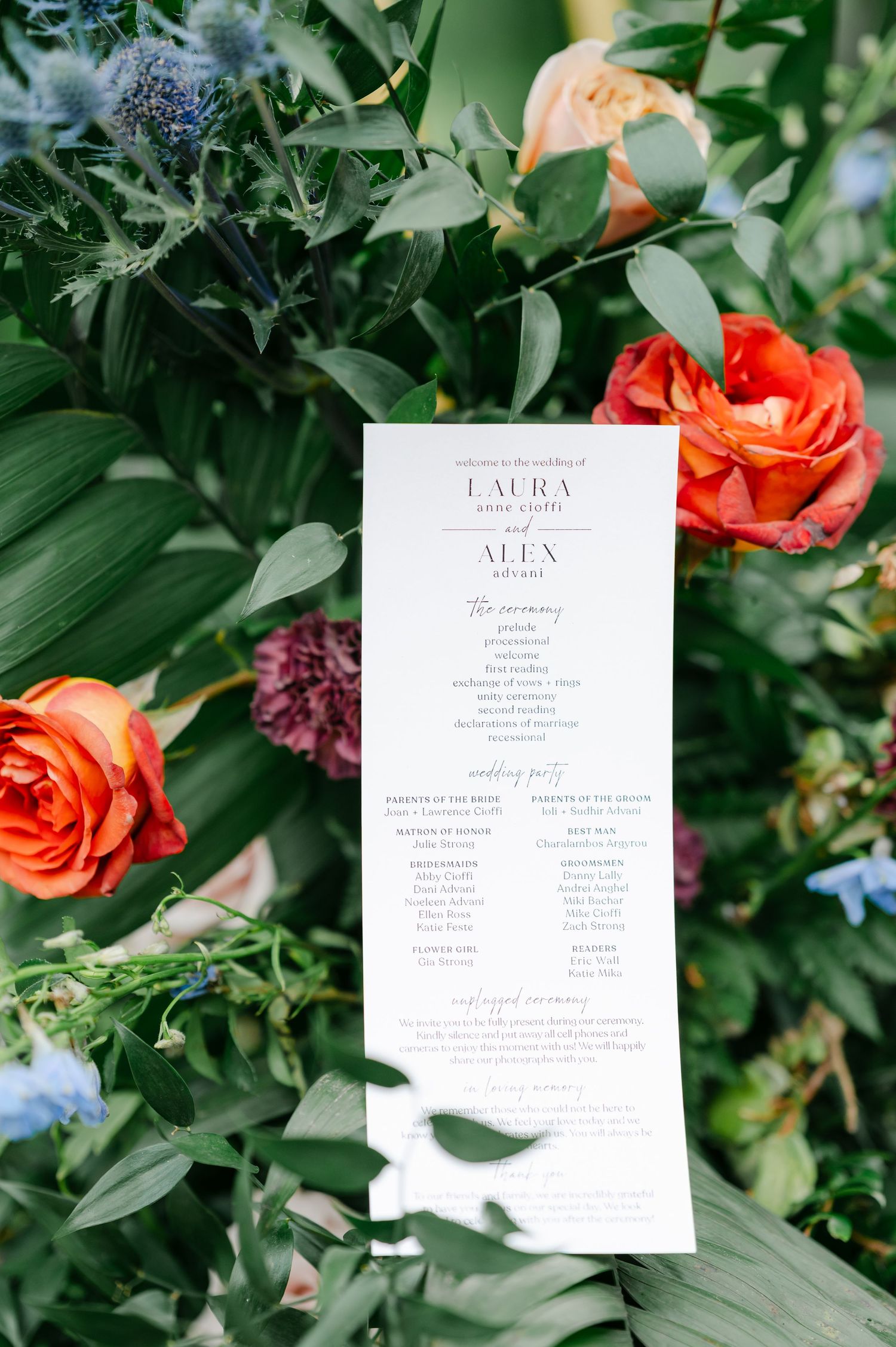 Wedding invitation cards displayed among green foliage and coral-colored roses in an elegant garden setting. - Hyatt Lodge Oak Brook