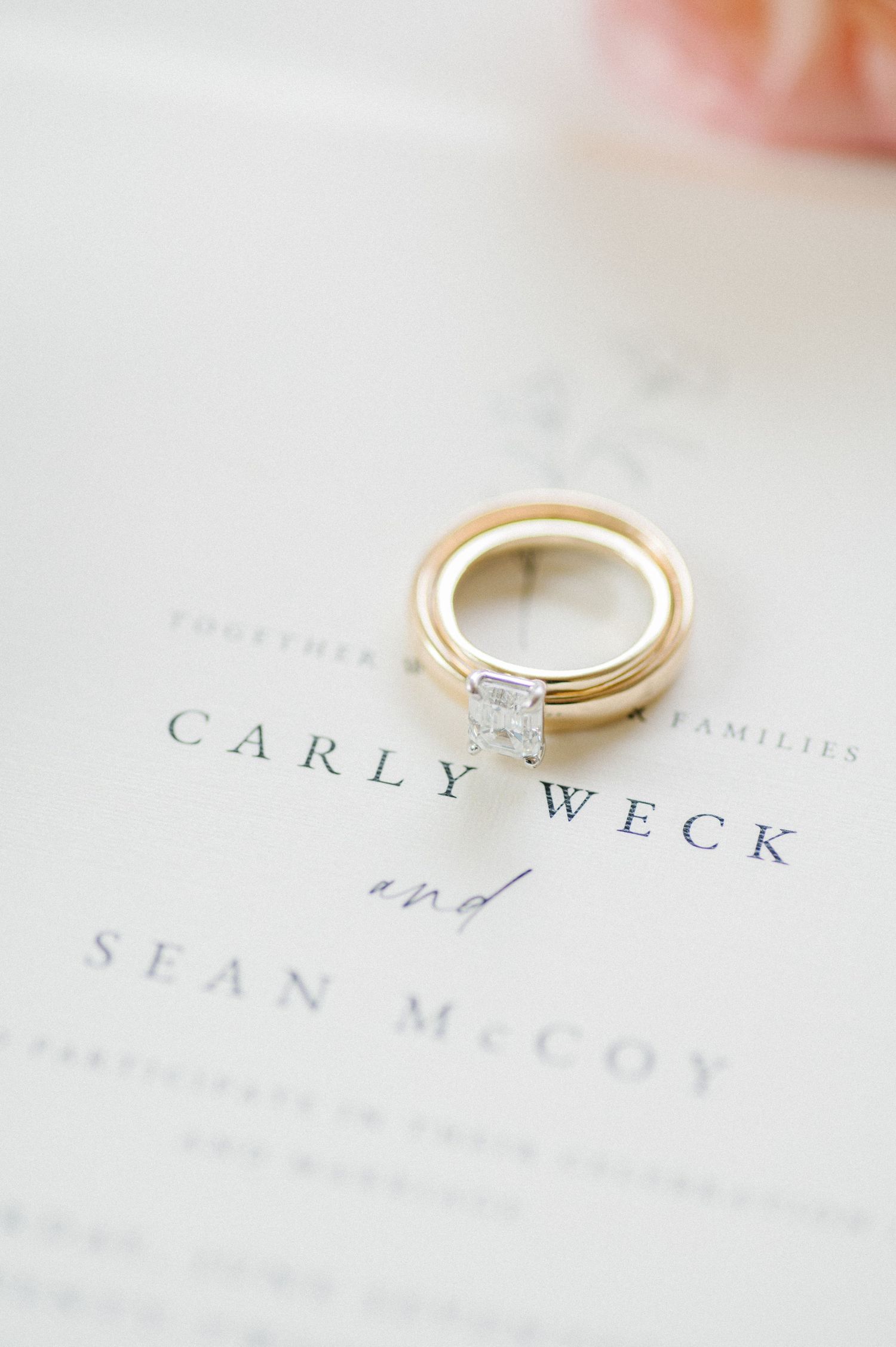 Wedding bands and engagement ring photographed on top of elegant wedding invitation printed with couples names.