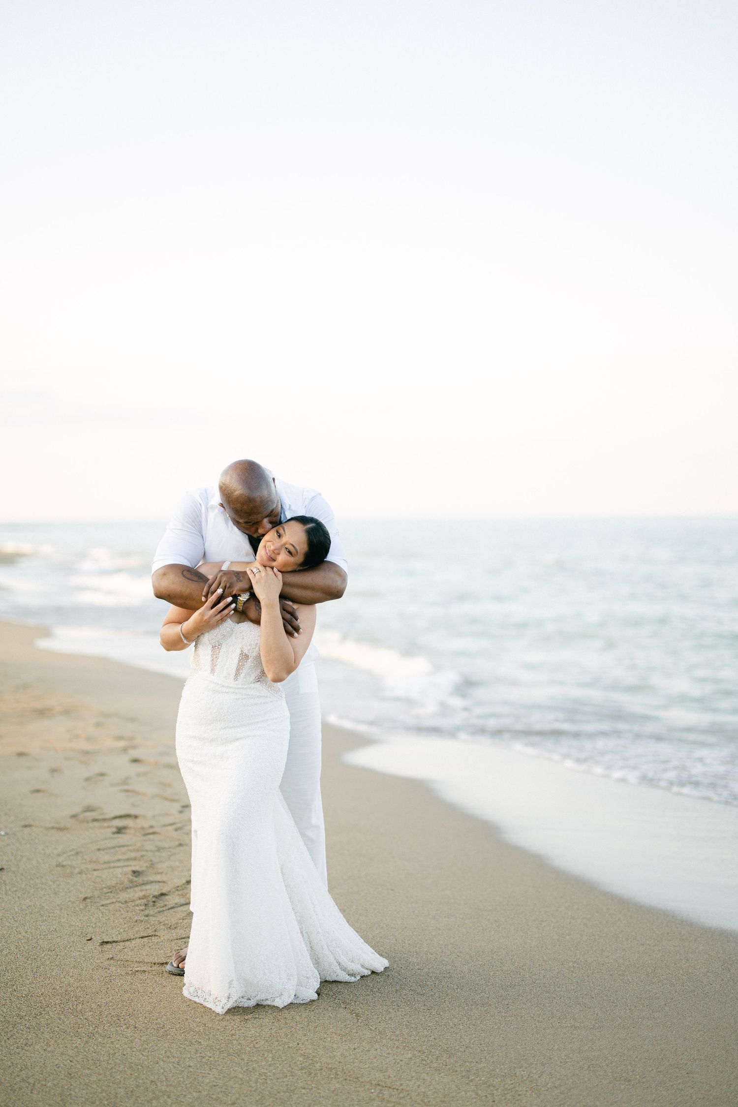 A romantic embrace between newlyweds on a sandy beach at sunset.