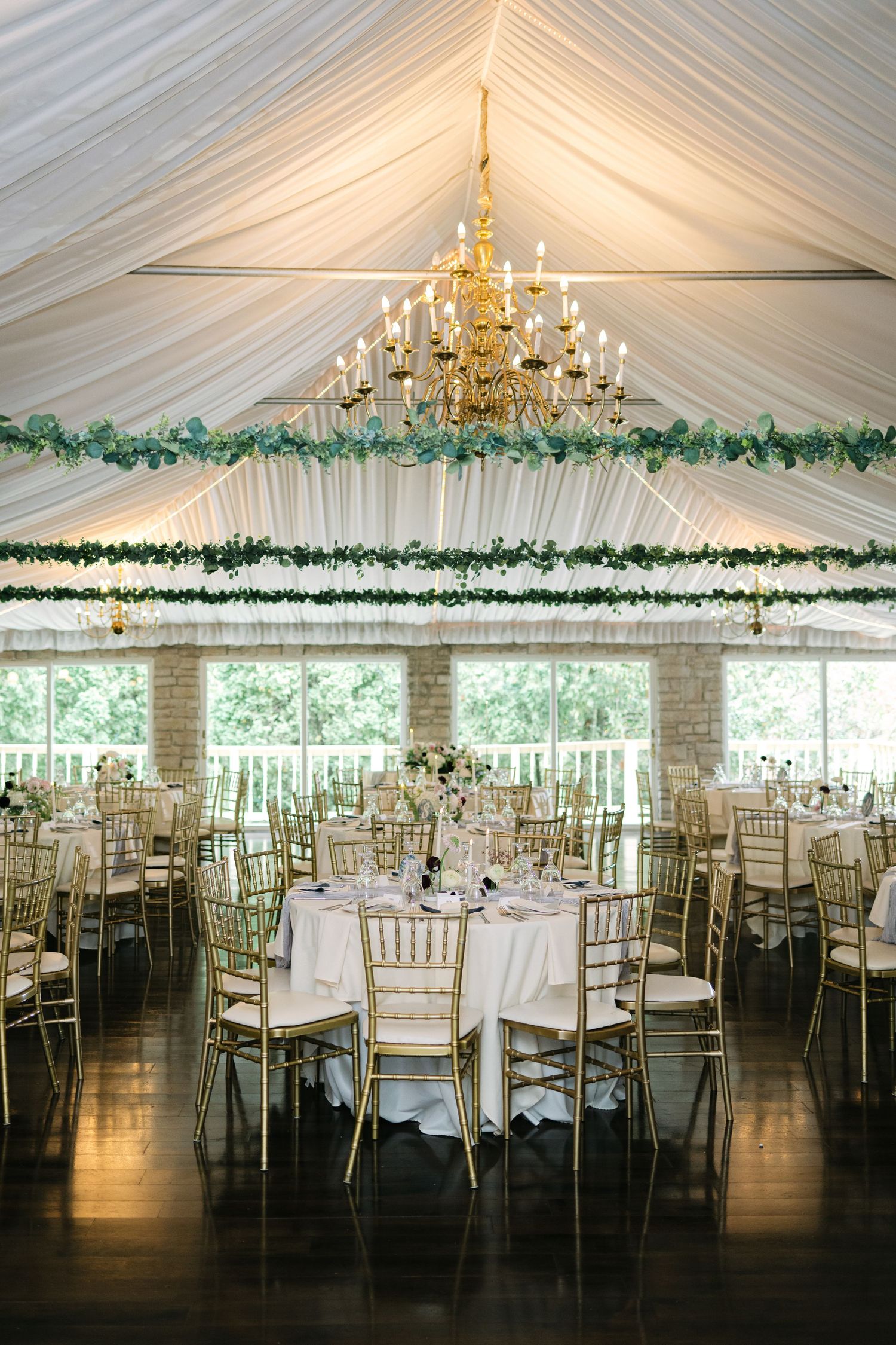 Elegant wedding reception venue with white tent draping, gold chandeliers, and green garland decorations along the ceiling. - Meyer's Castle