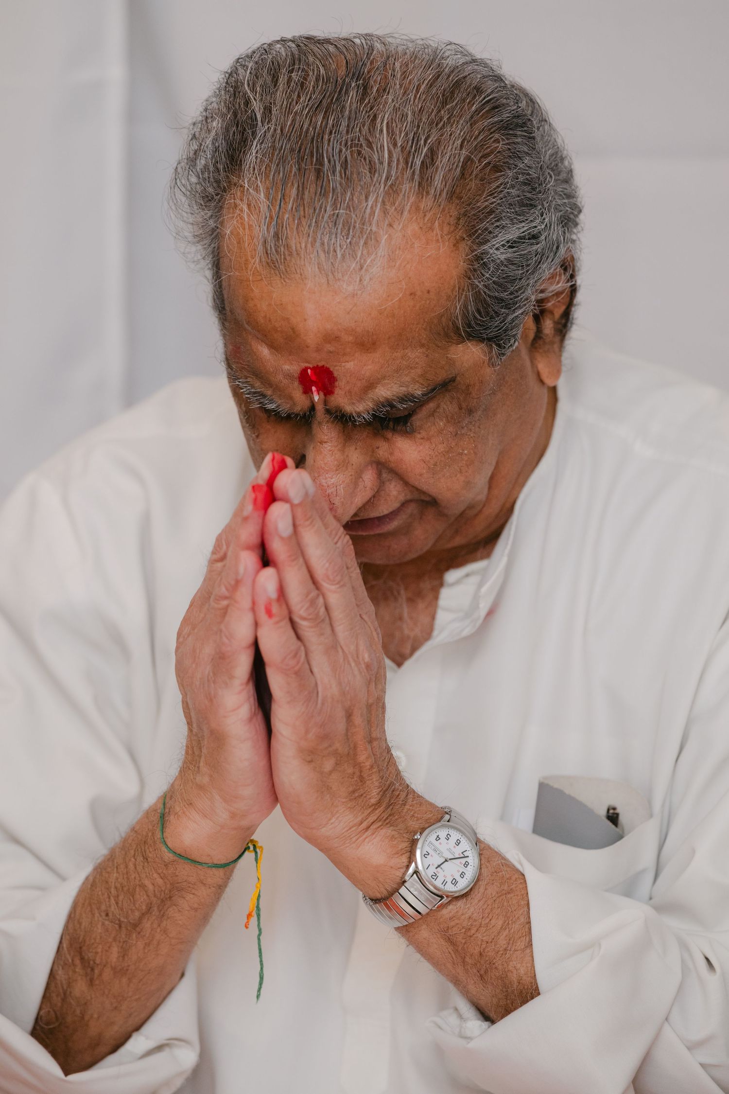 The Brix on the Fox Wedding - A person wearing white clothing and a wristwatch prays with hands clasped and a red mark on their forehead.