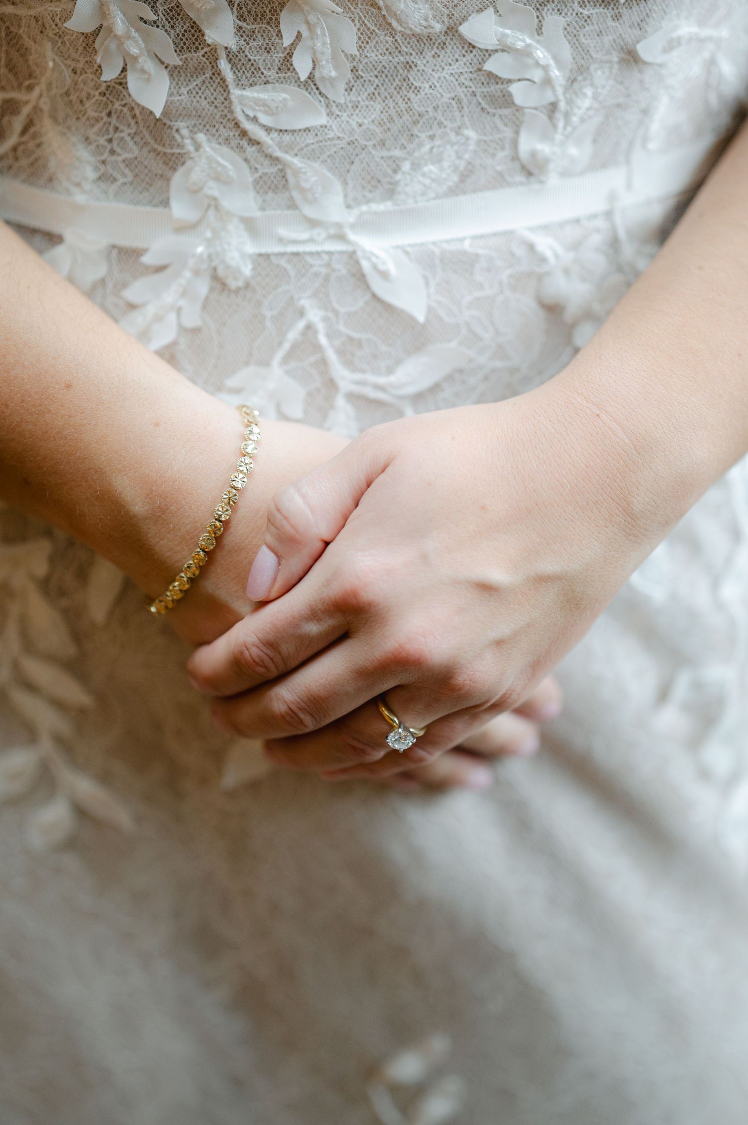 Close up of hands wearing delicate gold rings against white lace fabric background. - Hyatt Lodge Oak Brook