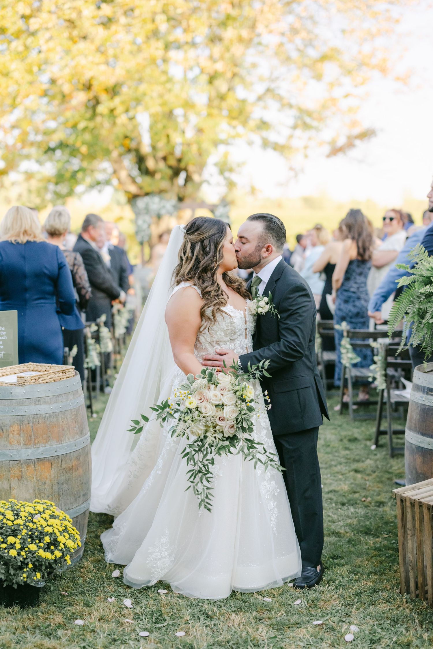 Bride and groom share first kiss at outdoor fall wedding ceremony. - Youngblood Vineyard Wedding