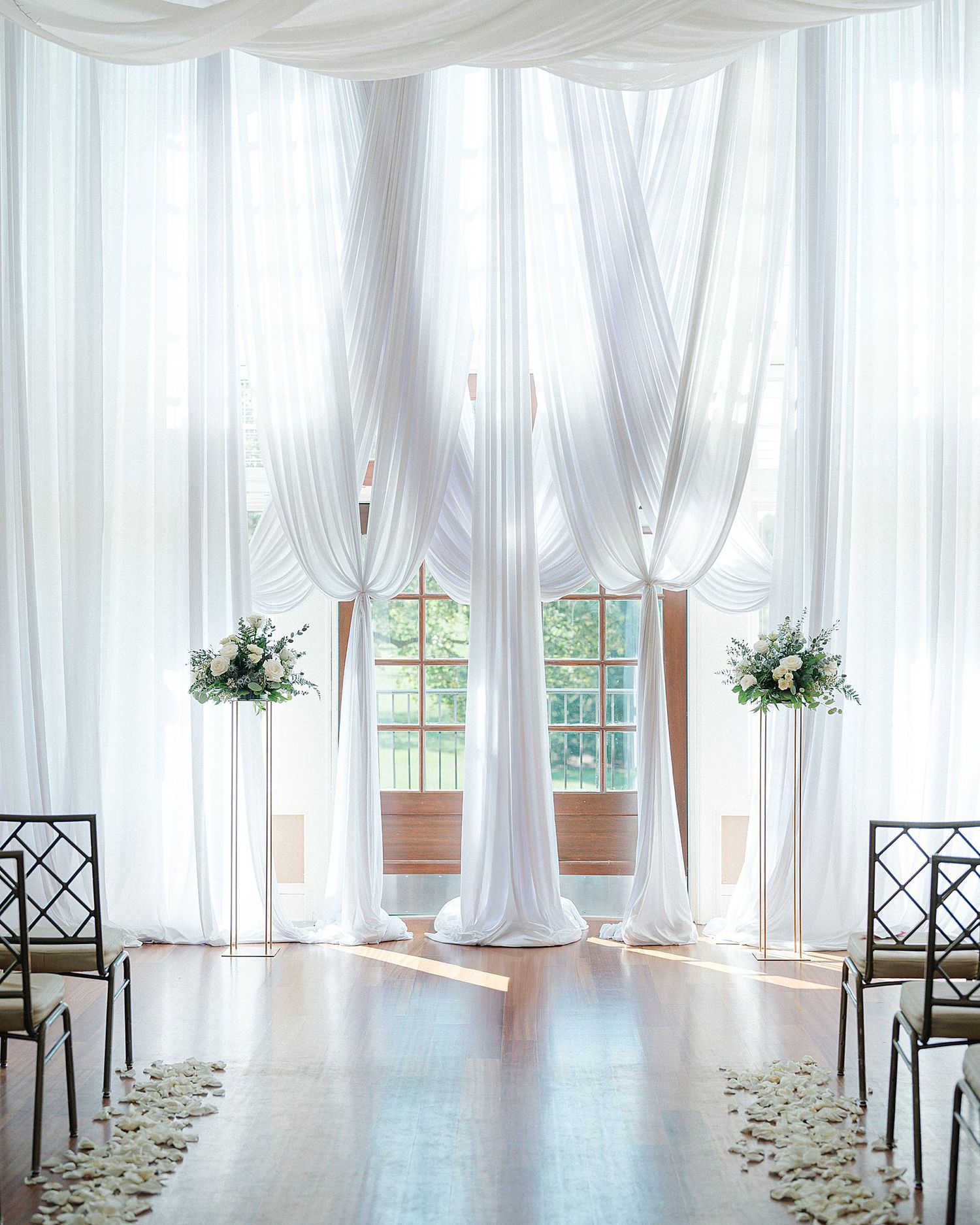 White draped fabric and flower arrangements line an elegant indoor ceremony space. - Ruffled Feathers Golf Club Wedding
