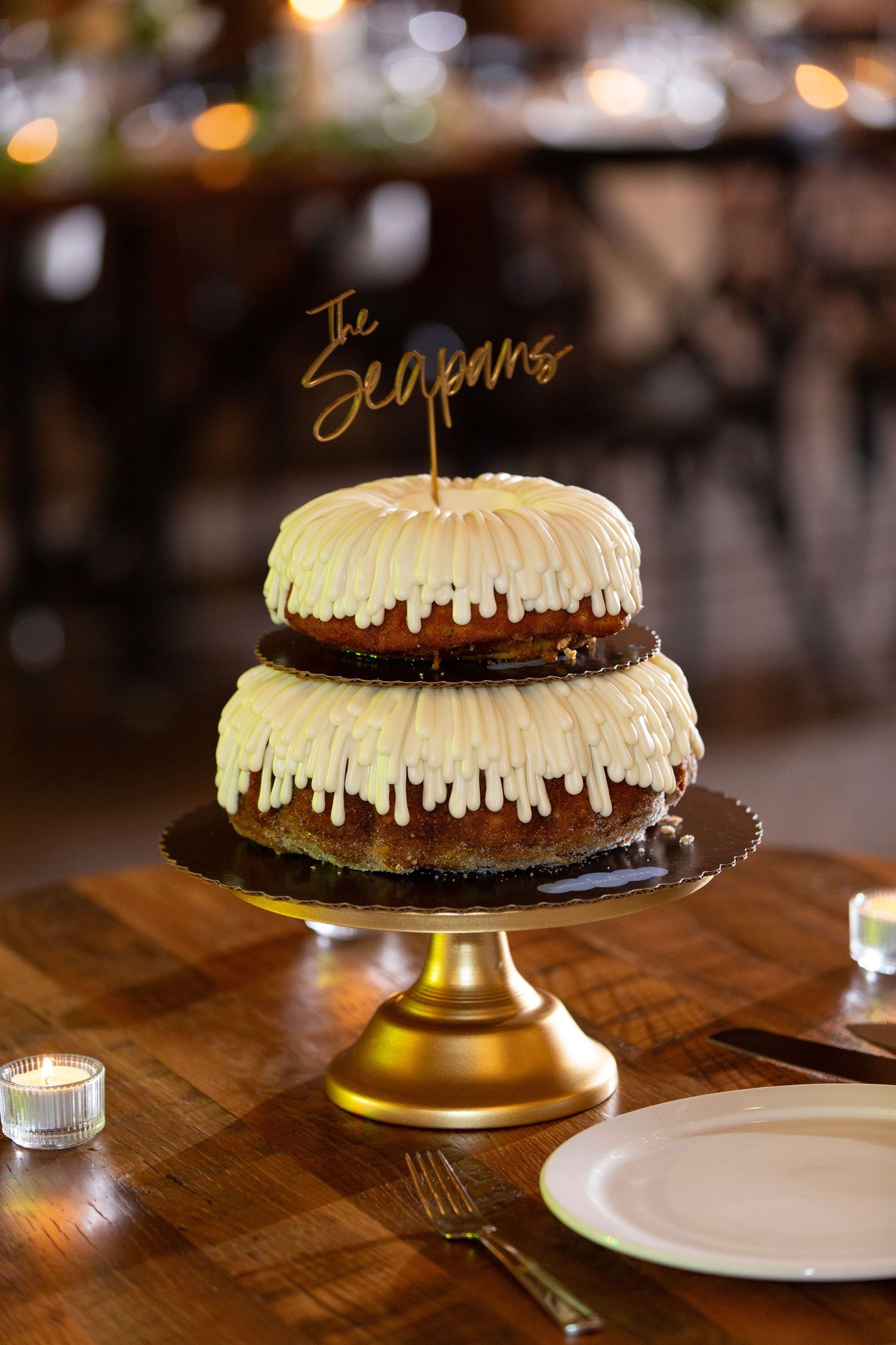 Chocolate bundt cakes with white frosting drips displayed on gold cake stands in a dimly lit restaurant setting. - The Bridge Lemont Wedding
