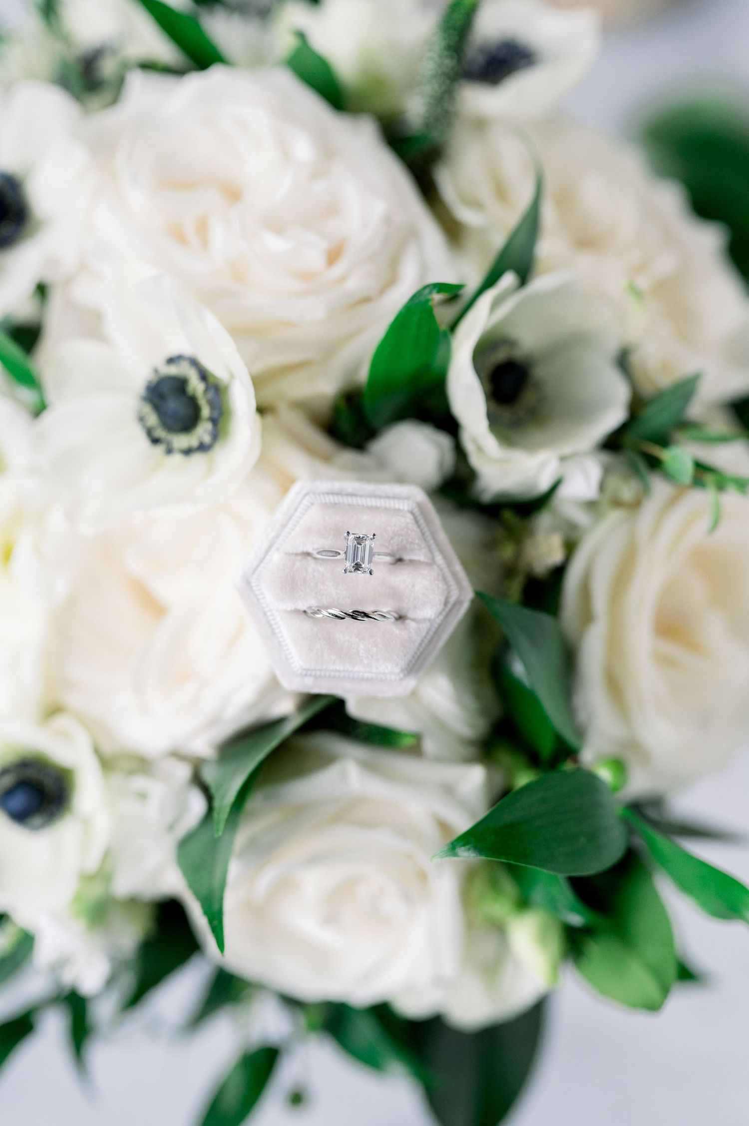Engagement ring in hexagonal box nestled among white roses and anemones.