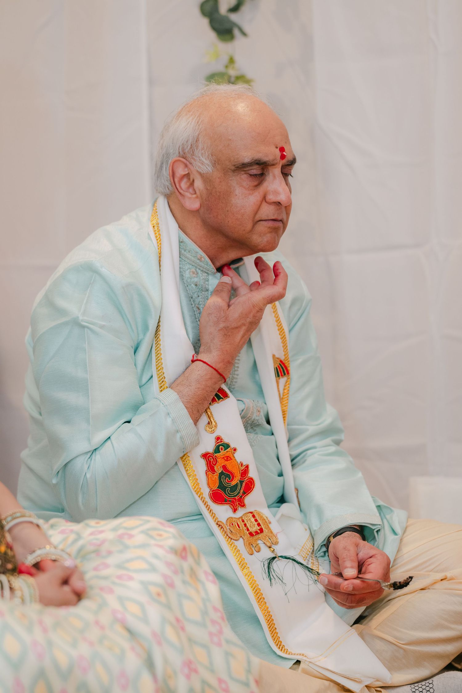 The Brix on the Fox Wedding - Elderly person in light blue traditional Indian attire sits in contemplative pose during ceremony.
