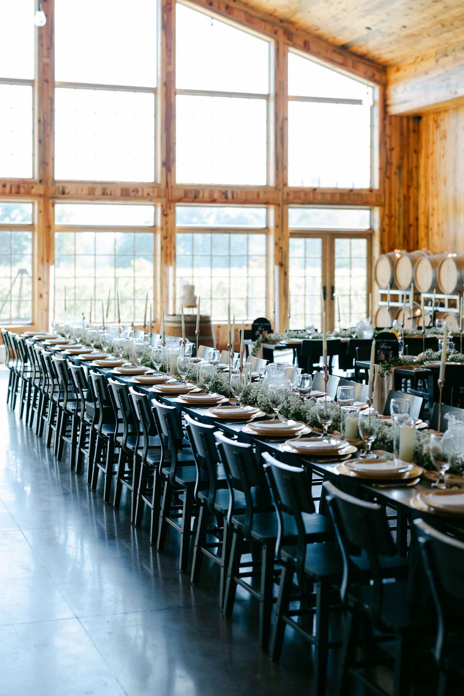 Elegant barn wedding reception with long tables, black chairs, greenery centerpieces. - Youngblood Vineyard Wedding