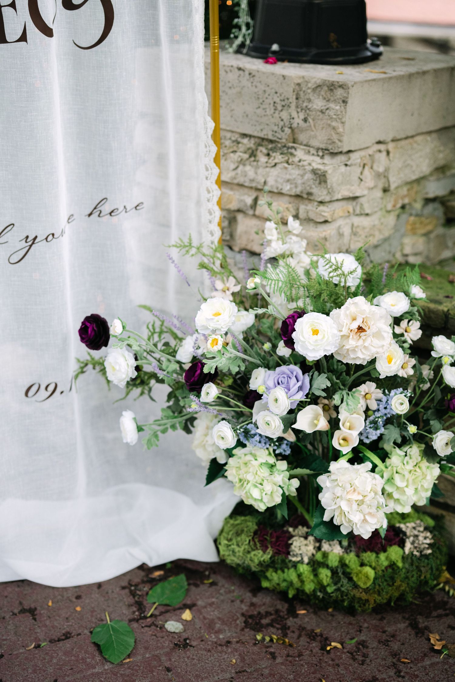 Delicate white and pink floral arrangements with hydrangeas and roses line the base of a white curtained window. - Meyer's Castle Events