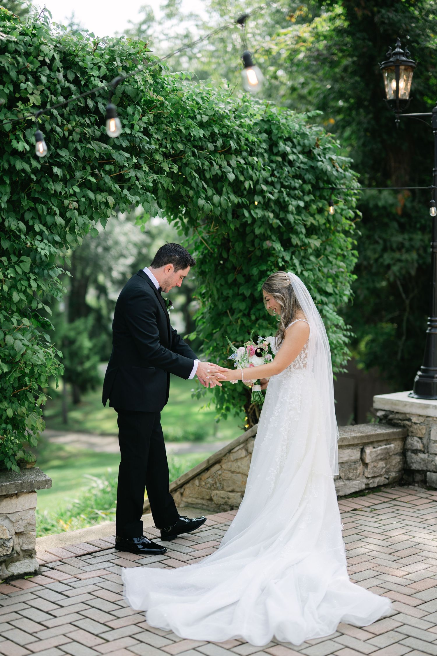A romantic wedding moment captured in a garden setting with a bride in white dress and groom on brick patio. - Meyer's Castle Events