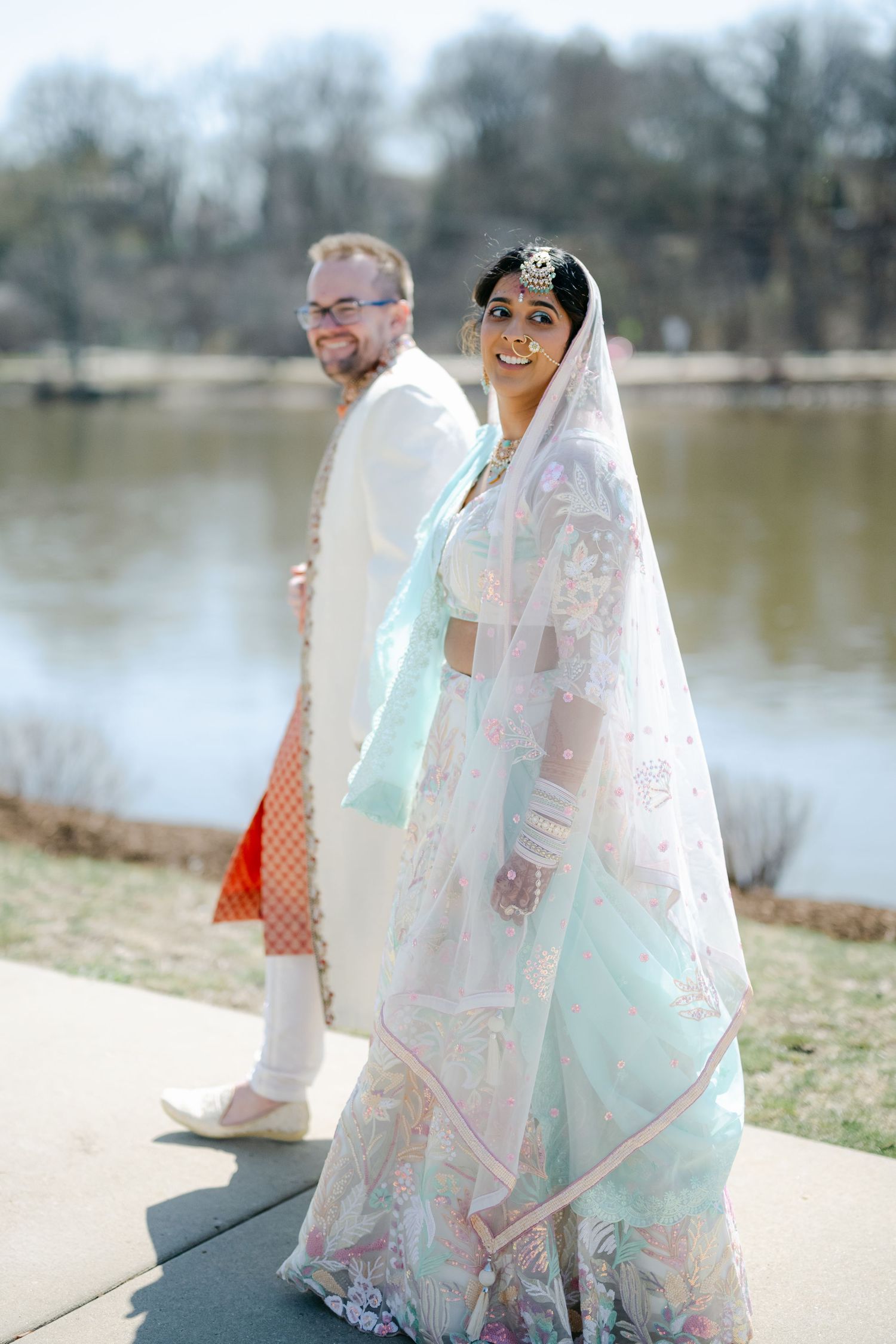 A couple in traditional South Asian wedding attire poses by a lakeside in a series of romantic photos. - The Brix on the Fox