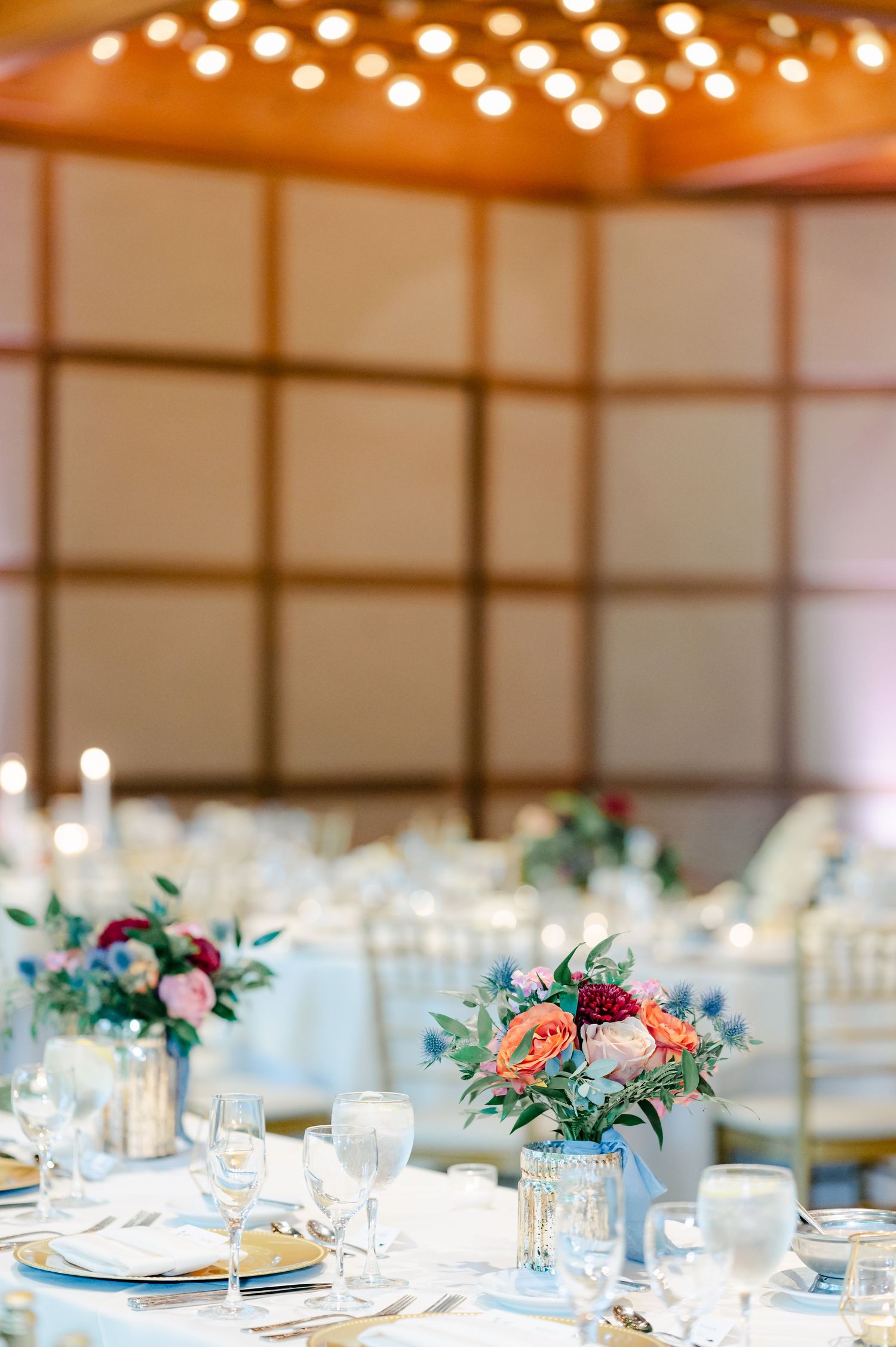 Elegant wedding reception table setting with coral and burgundy floral centerpieces and soft lighting from above. - Hyatt Lodge Oak Brook