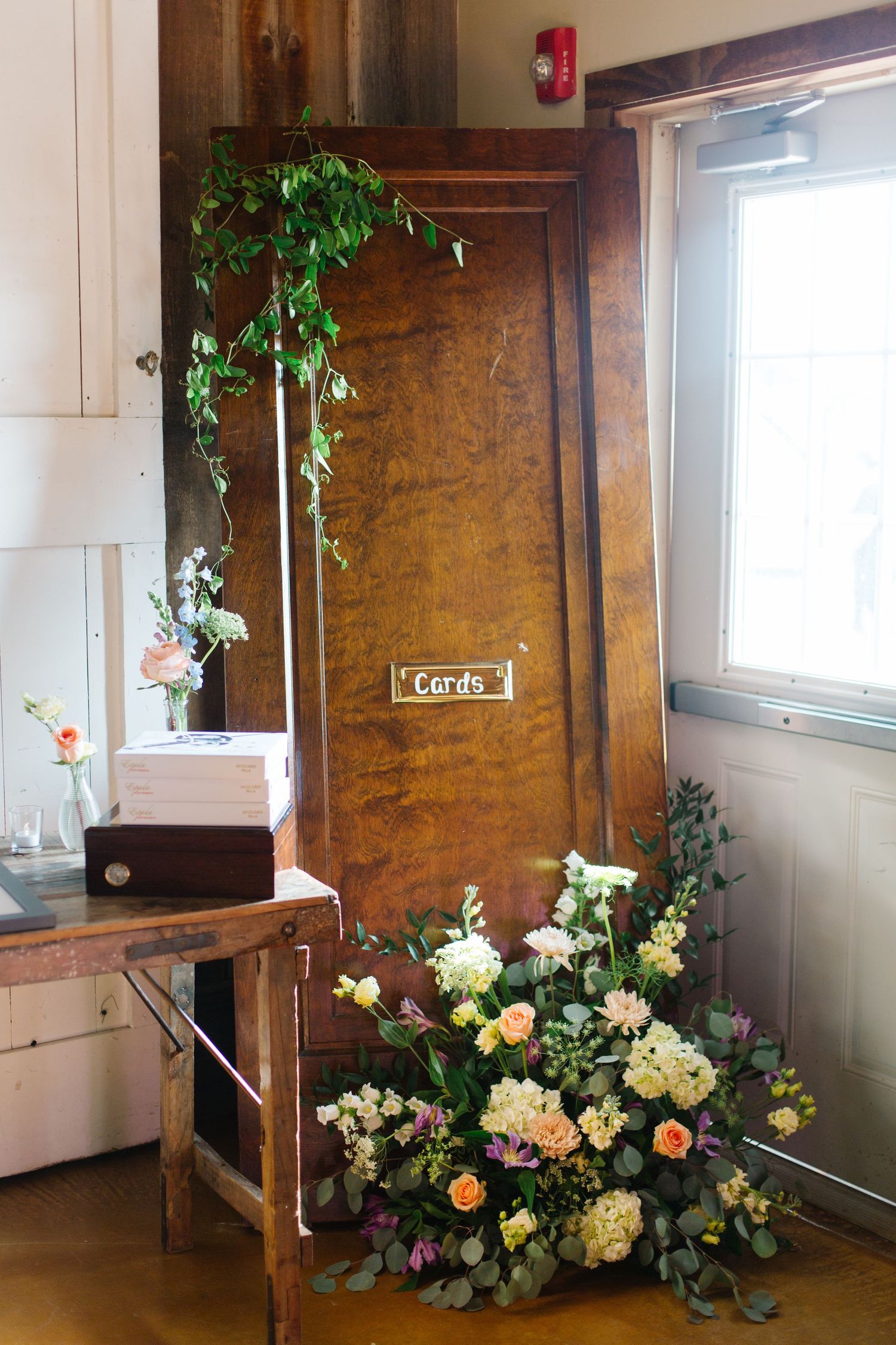 A rustic wooden door with a carpe sign is decorated with a flourishing floral arrangement and hanging green vines.
