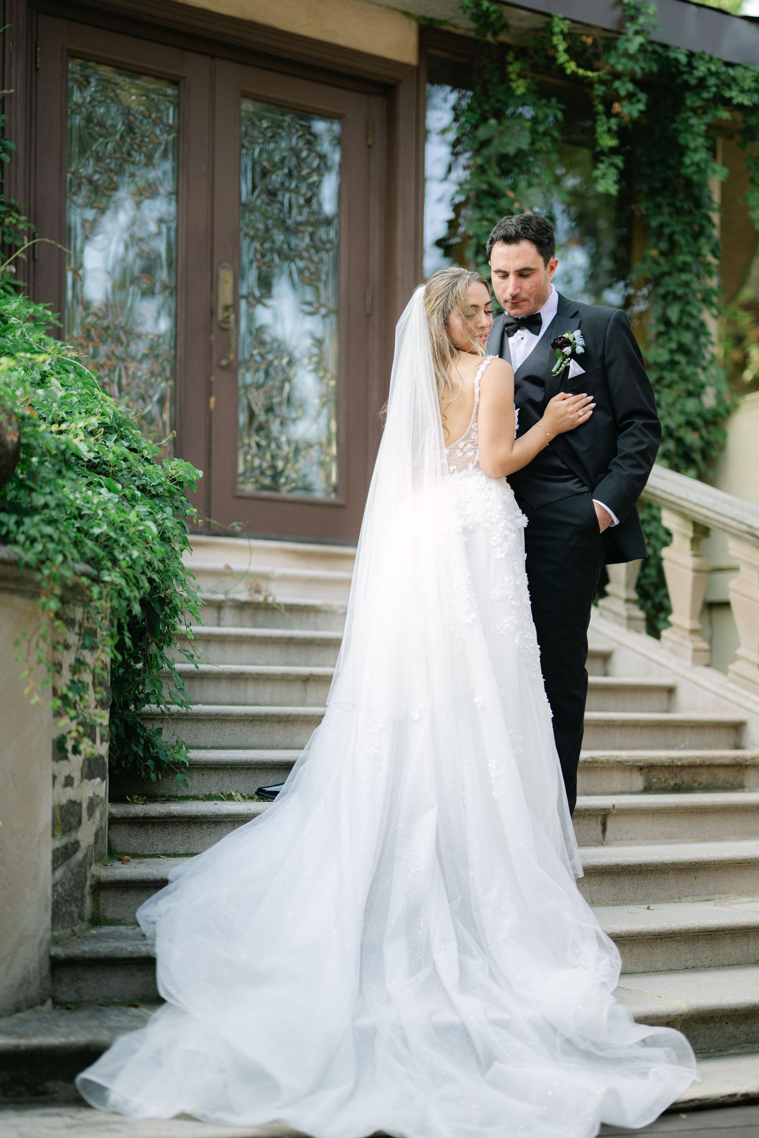 A romantic wedding couple shares intimate moments on elegant stone steps surrounded by lush greenery. - Meyer's Castle Events