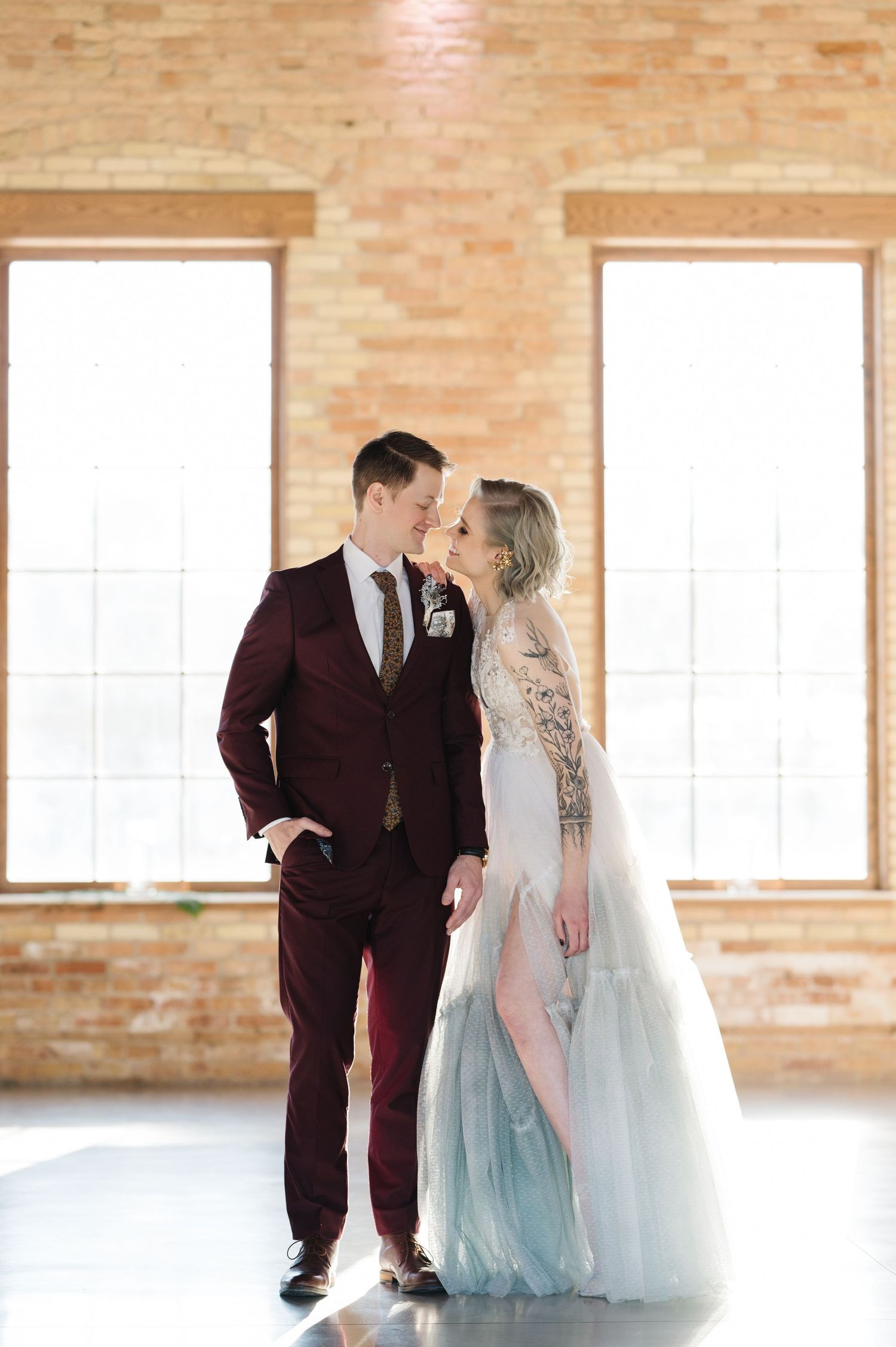A couple in formal wedding attire share an intimate moment in a bright industrial space with exposed brick walls.  - The Brix on the Fox