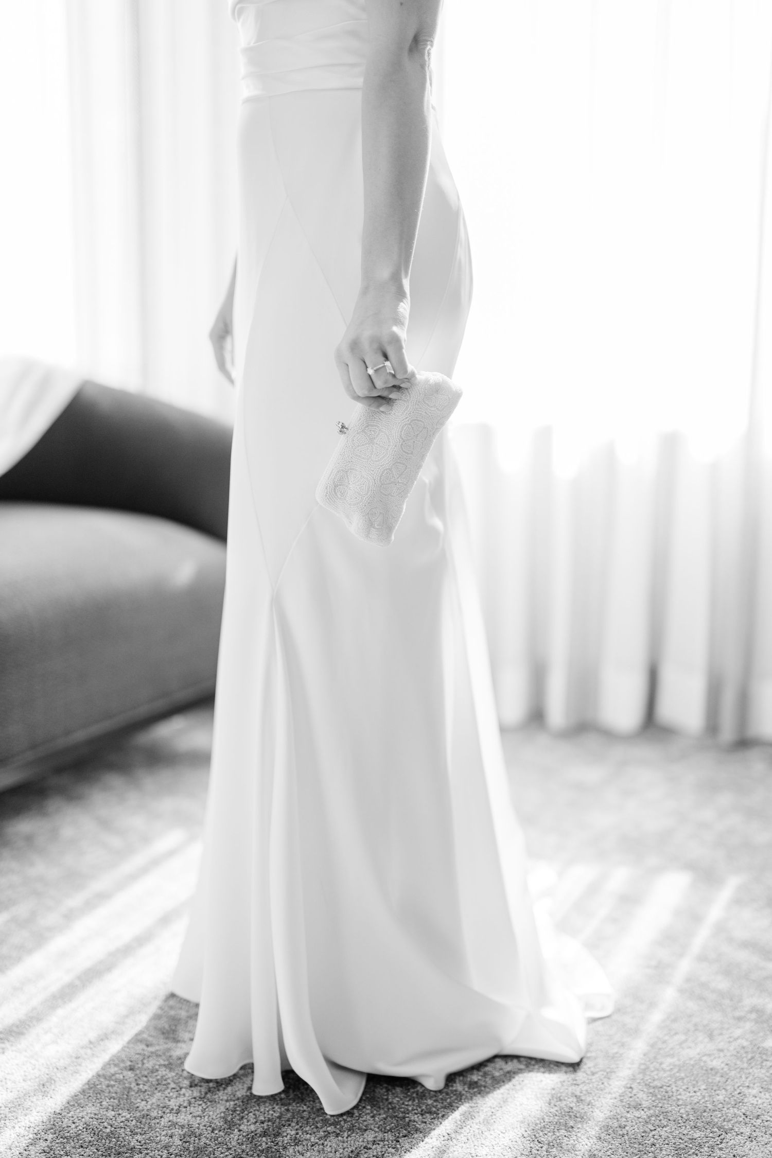 Black and white detail shot of flowing white wedding dress against window light.