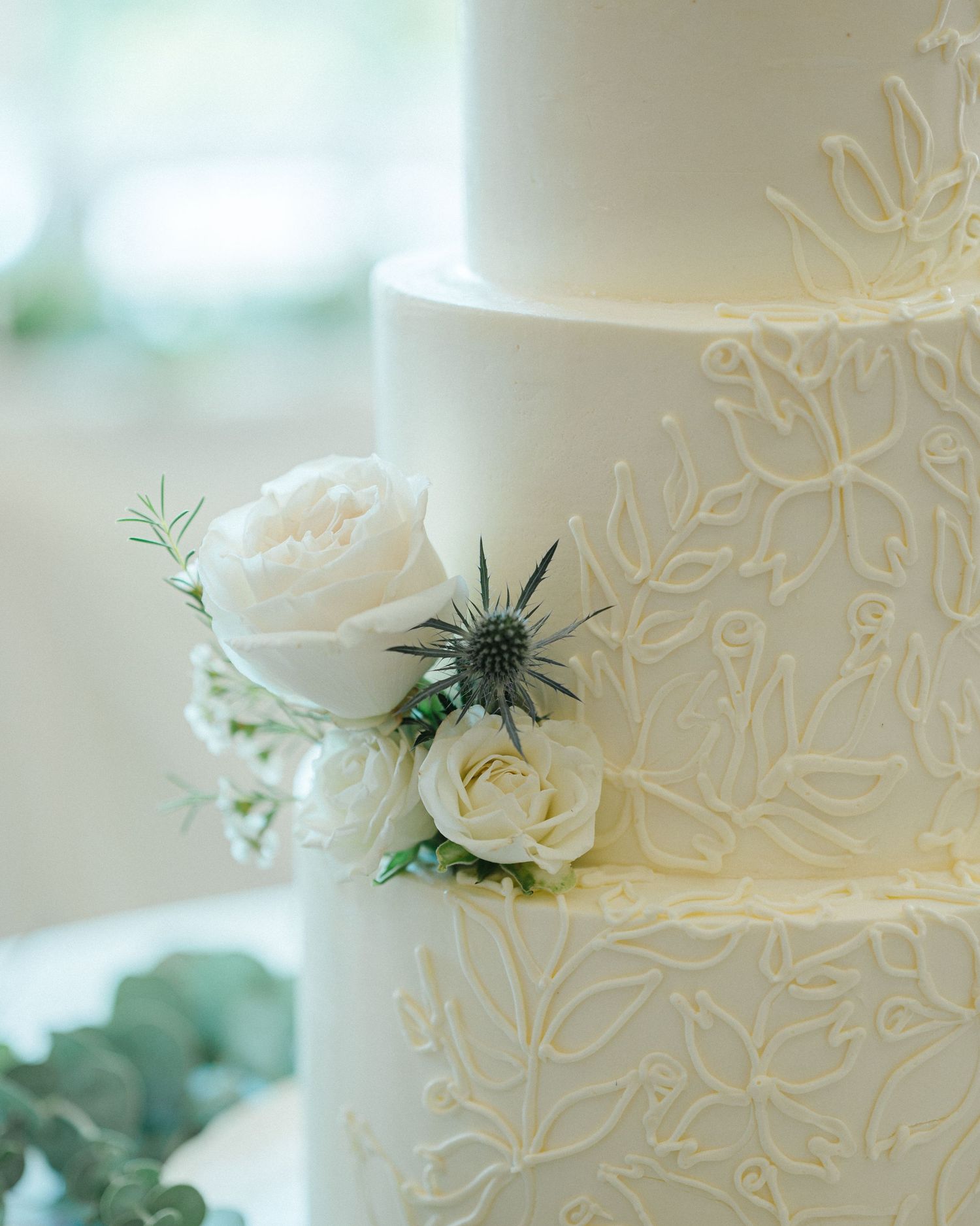 Close-up detail of an elegant white wedding cake with delicate floral embossing and fresh white rose accents. - Ruffled Feathers Golf Club