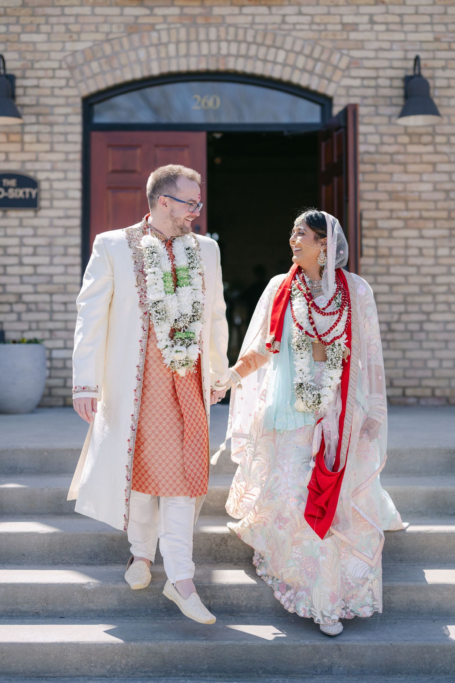 The Brix on the Fox Wedding - A couple in traditional Indian wedding attire walks together on a brick-lined sidewalk.