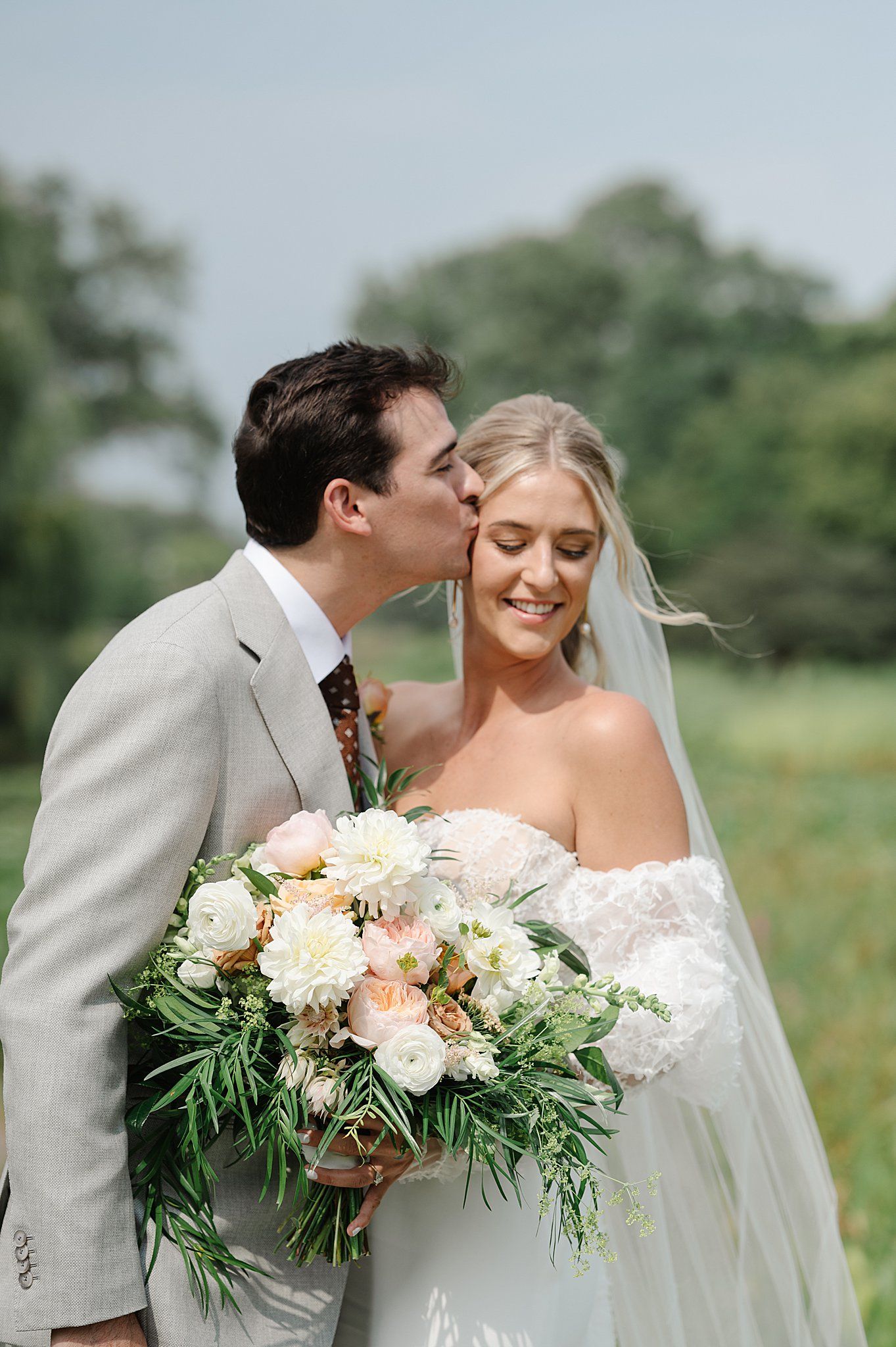 A romantic wedding moment outdoors with a beautiful floral bouquet featuring white and peach blooms with greenery.