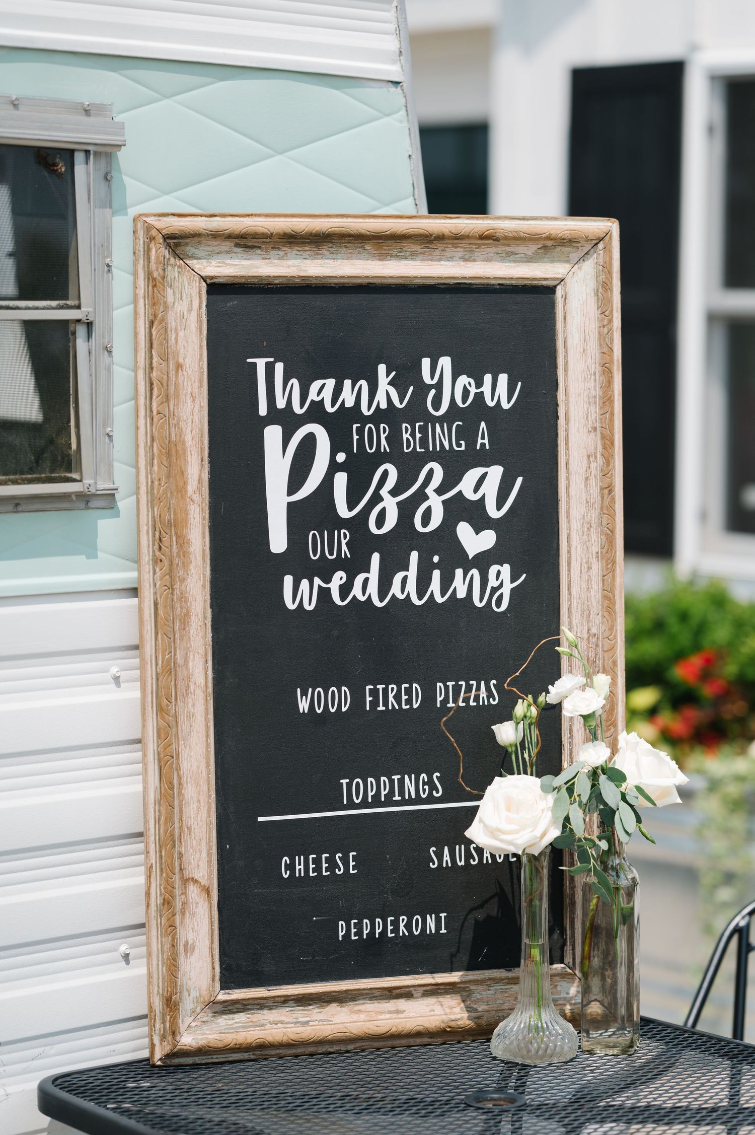 Rustic framed chalkboard wedding sign for pizza menu with white calligraphy text and small floral arrangement. - Venue 5126