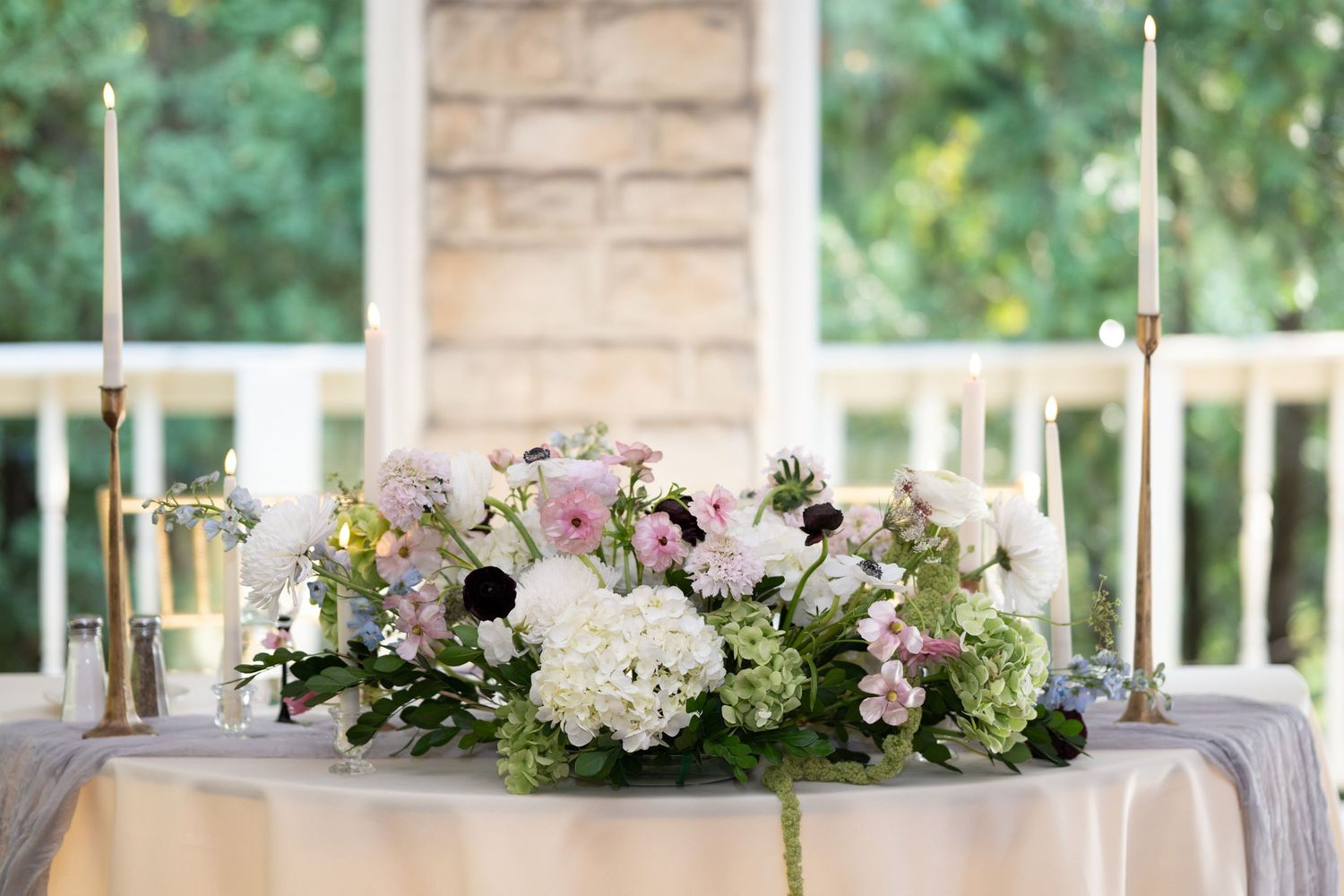Elegant wedding reception table with white hydrangeas and pink floral centerpieces on a rustic outdoor porch. - Meyer's Castle Events