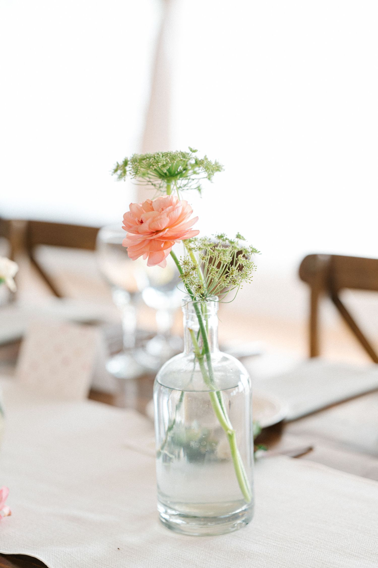 Simple wedding reception centerpiece with pink carnation and baby's breath in a clear glass bottle vase.