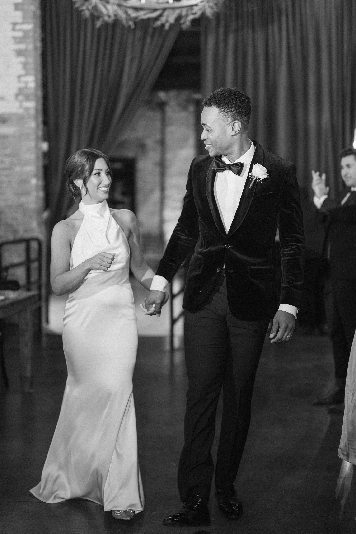 A couple in wedding attire holds hands and smiles at each other during a black and white reception moment. - Sanctuary Events Plainfield