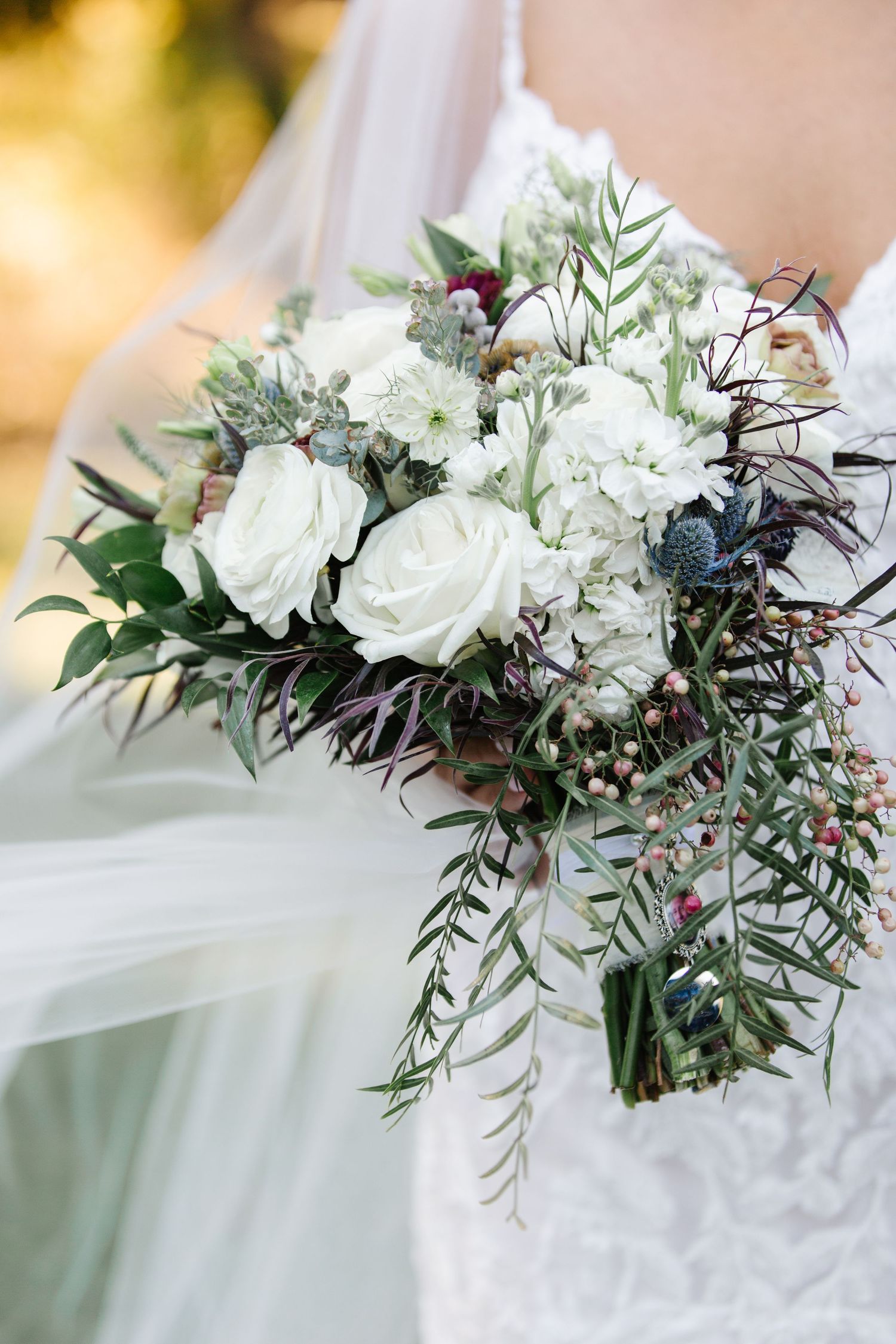White roses and eucalyptus wedding bouquet with dark foliage accents creates elegant contrast in natural lighting.