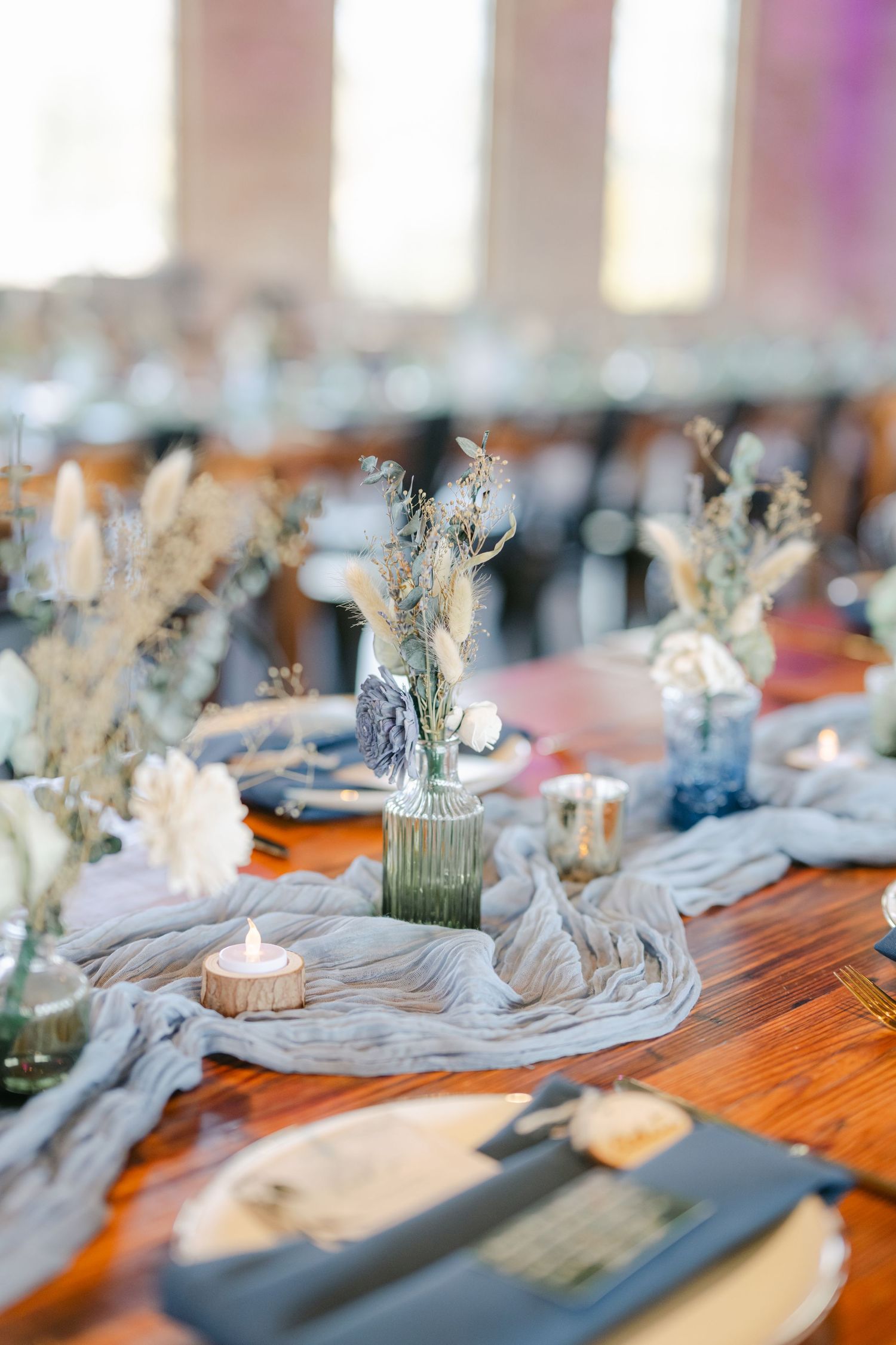 Elegant table settings with candles and dried flowers create a rustic wedding reception atmosphere on wooden tables. - The Brix on the Fox