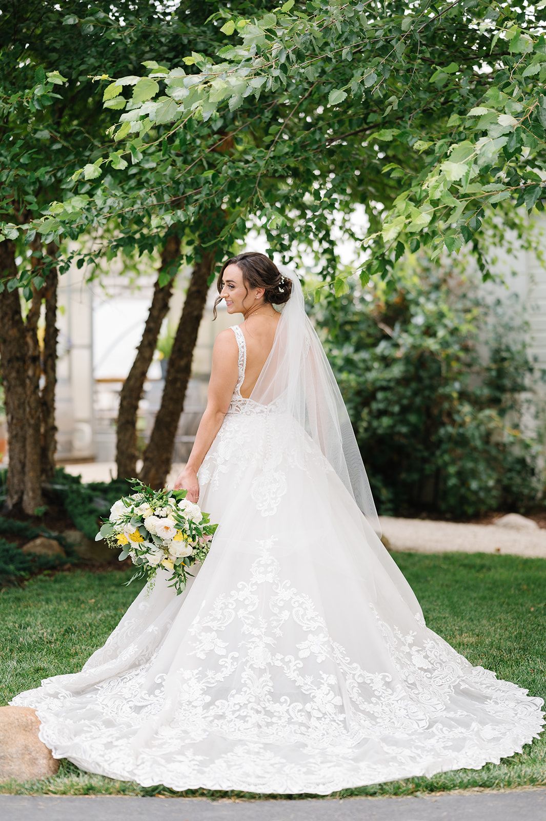 Bride in lace ballgown with veil holding yellow and white bouquet. - Heritage Prairie Farm Wedding