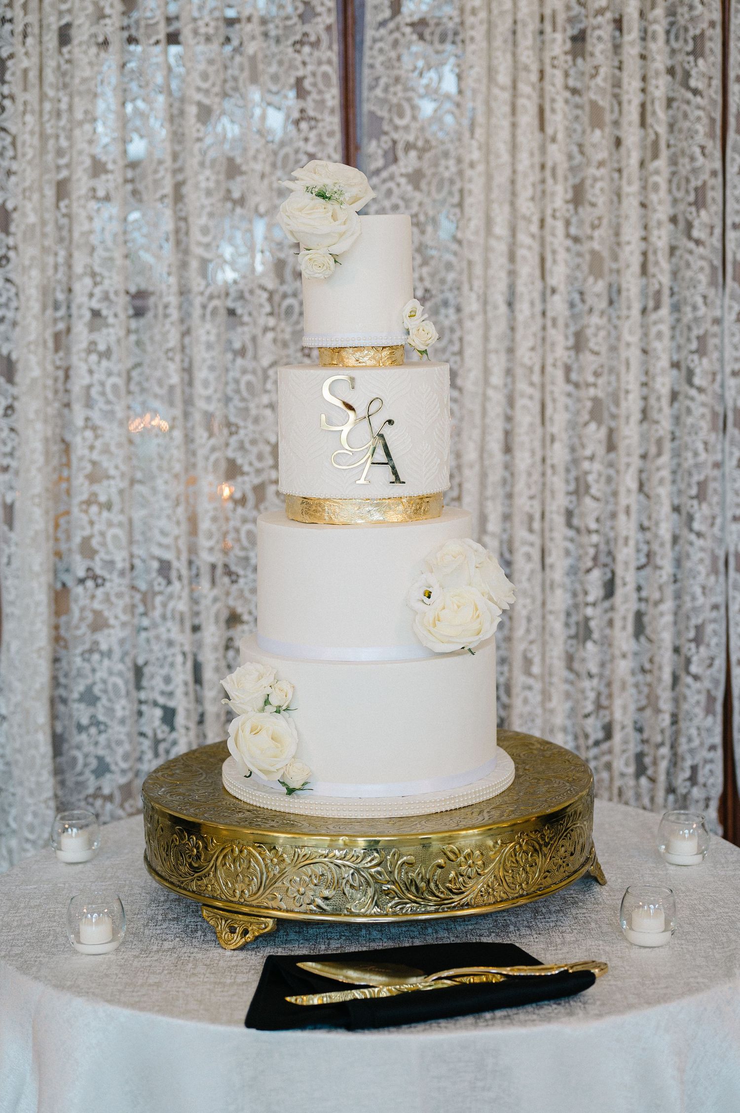 Three-tiered white wedding cake with gold accents displayed on ornate gold cake stand. - The Armour House in Lake Forest