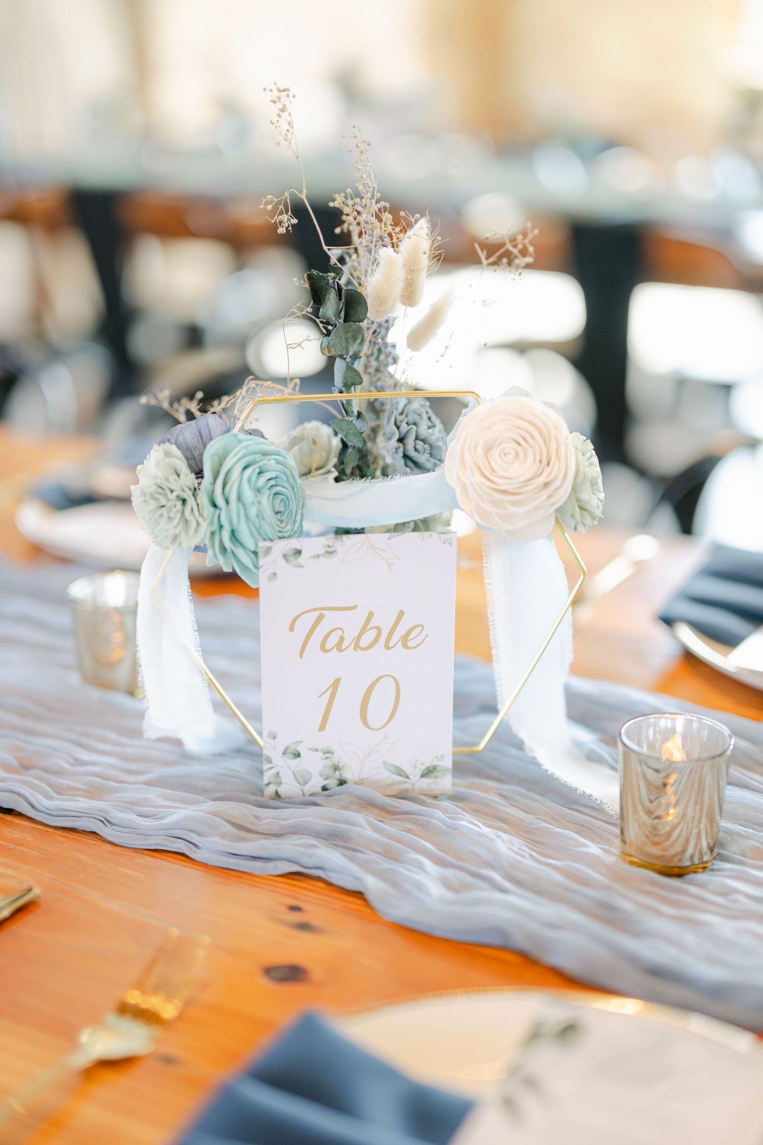 Elegant wedding table settings with soft blue and white floral centerpieces and gold table number cards. - The Brix on the Fox