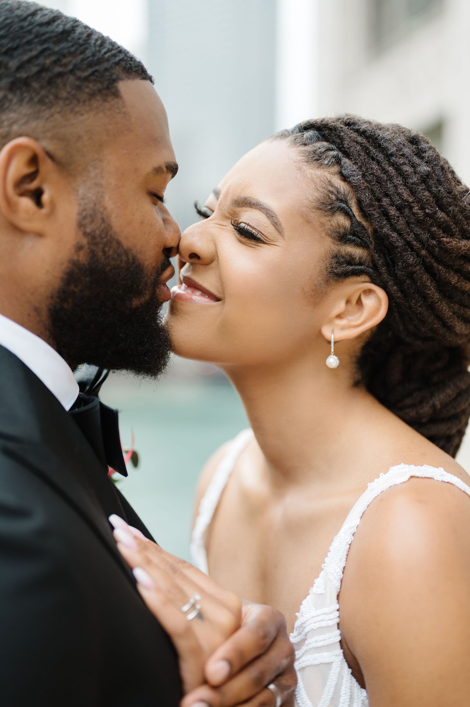A tender wedding moment between a couple in formal attire sharing a romantic kiss against a light-colored backdrop. - Ovation Chicago